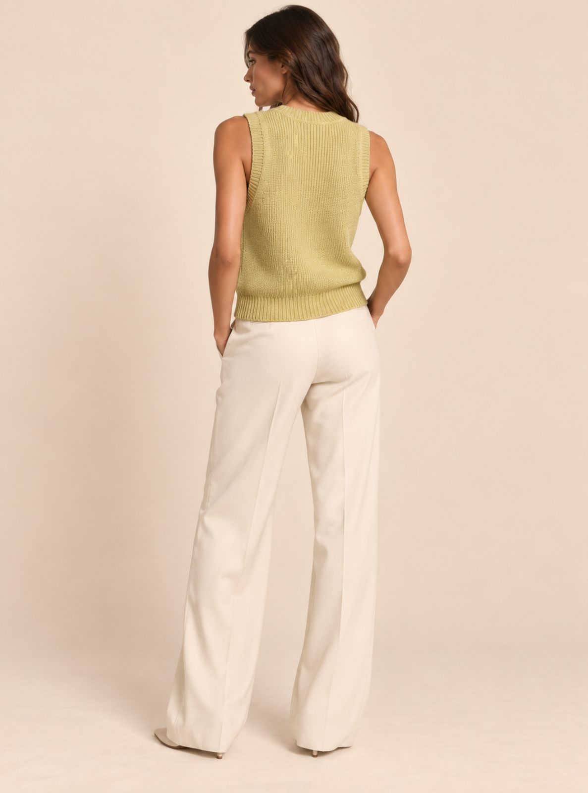 A woman shown from the back wearing a sleeveless ribbed knit vest in a pale yellow-green and off-white wide-leg pants, standing against a solid beige studio background.
