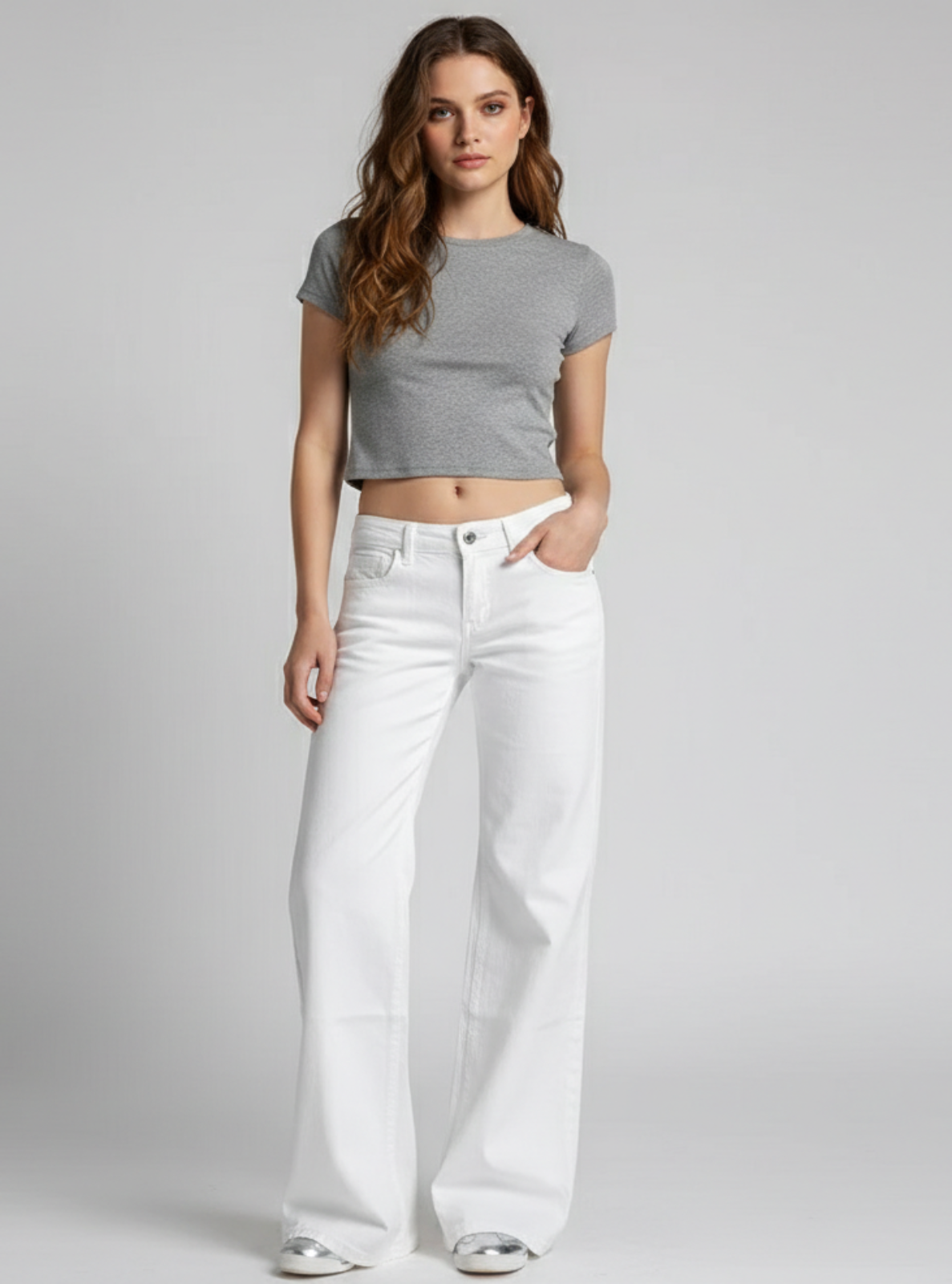 Woman wearing a gray crop top and white wide-leg jeans on a plain background