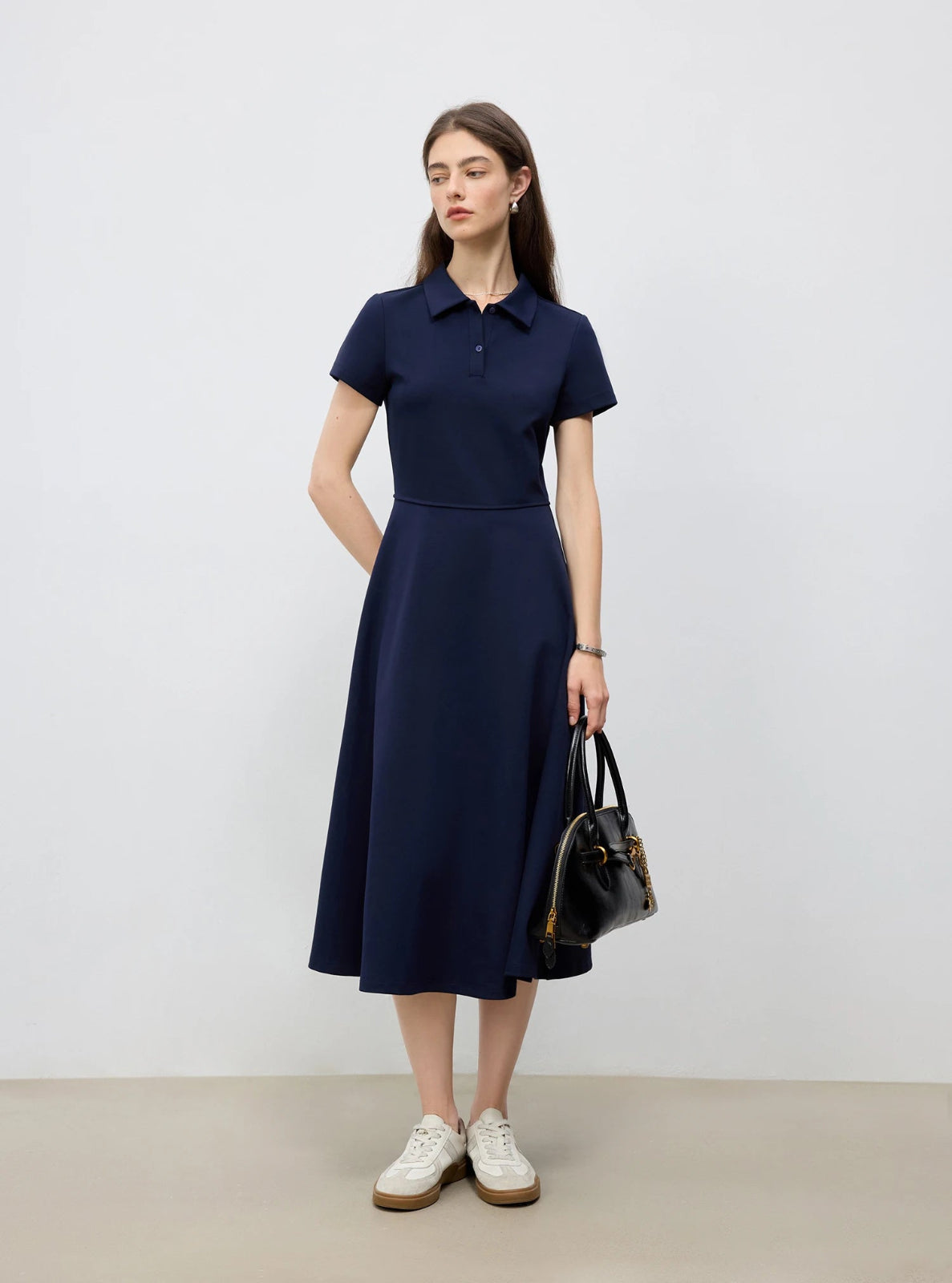 Woman wearing a navy dress holding a black handbag against a white background