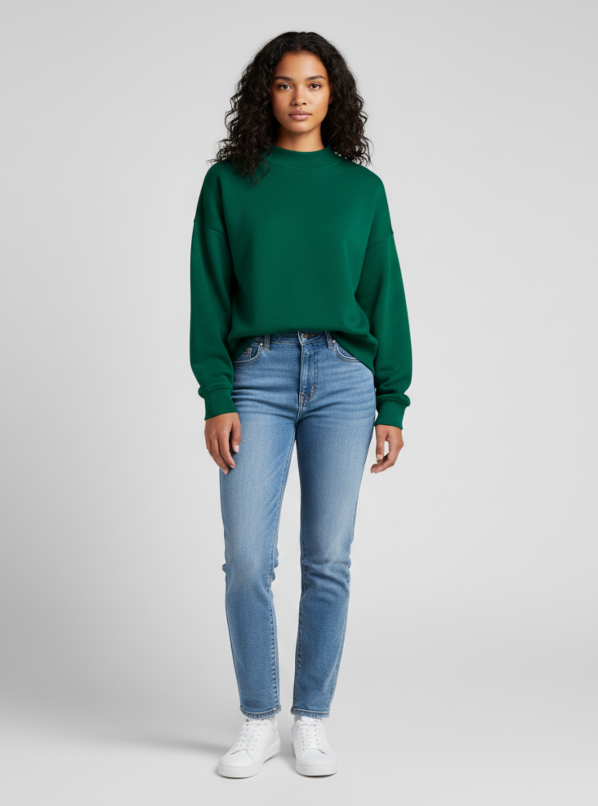 Woman wearing a green sweater and blue jeans on a gray background