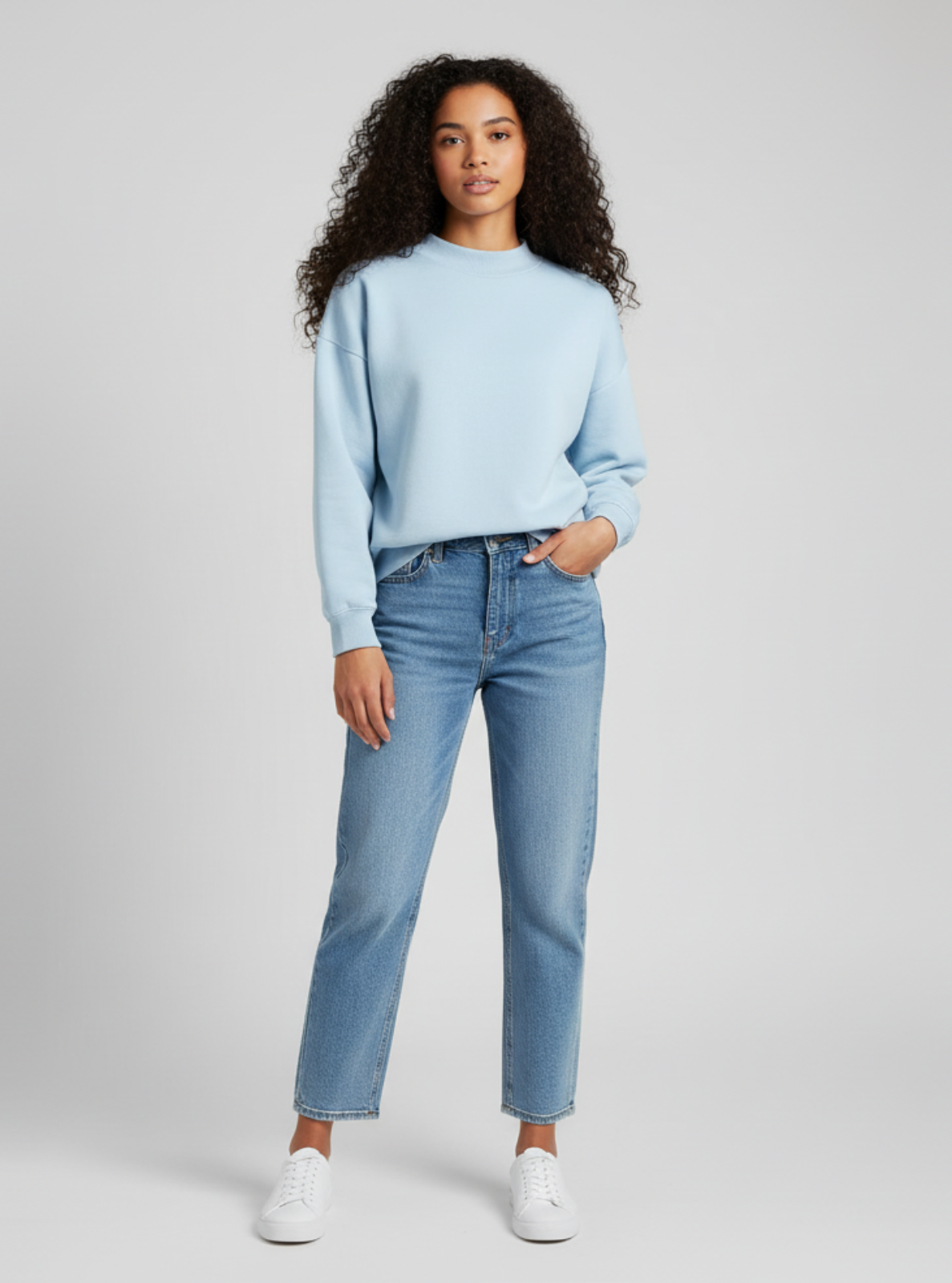 Woman wearing a light blue sweater and jeans on a gray background