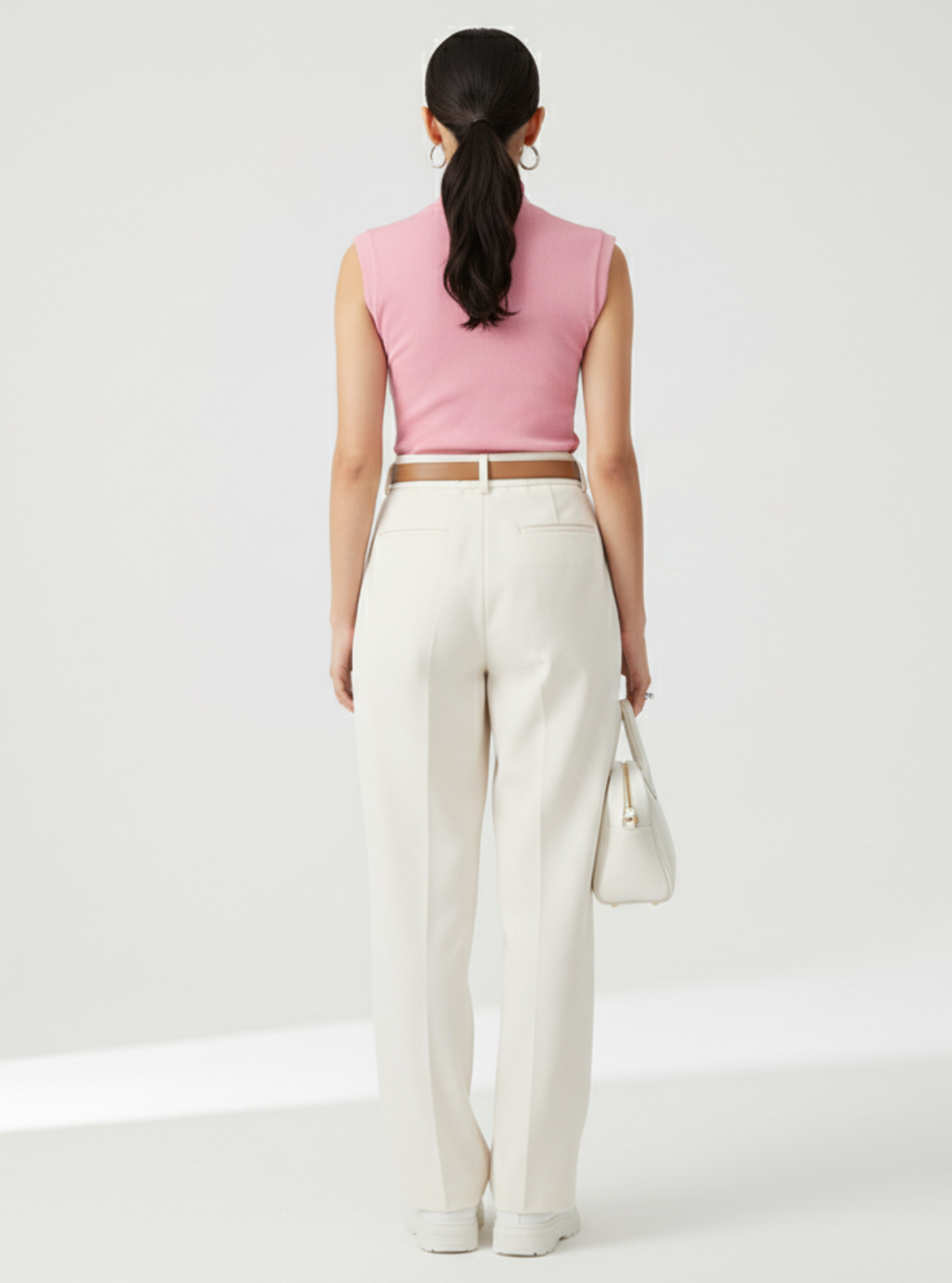 Woman wearing a pink sleeveless top and white pants on a light gray background