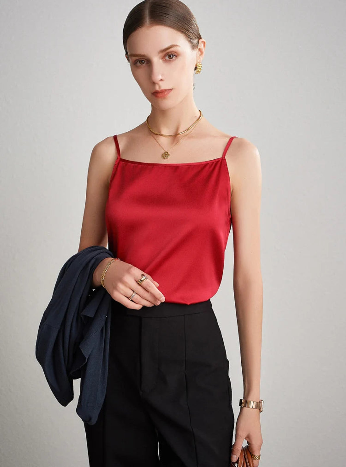 Woman wearing a red top and black pants against a gray background