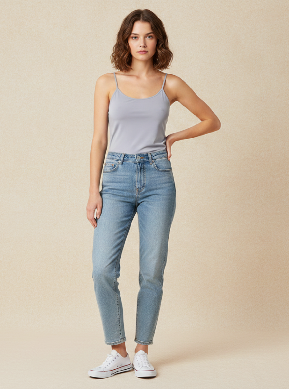 Woman wearing light blue jeans and a gray tank top against a beige background