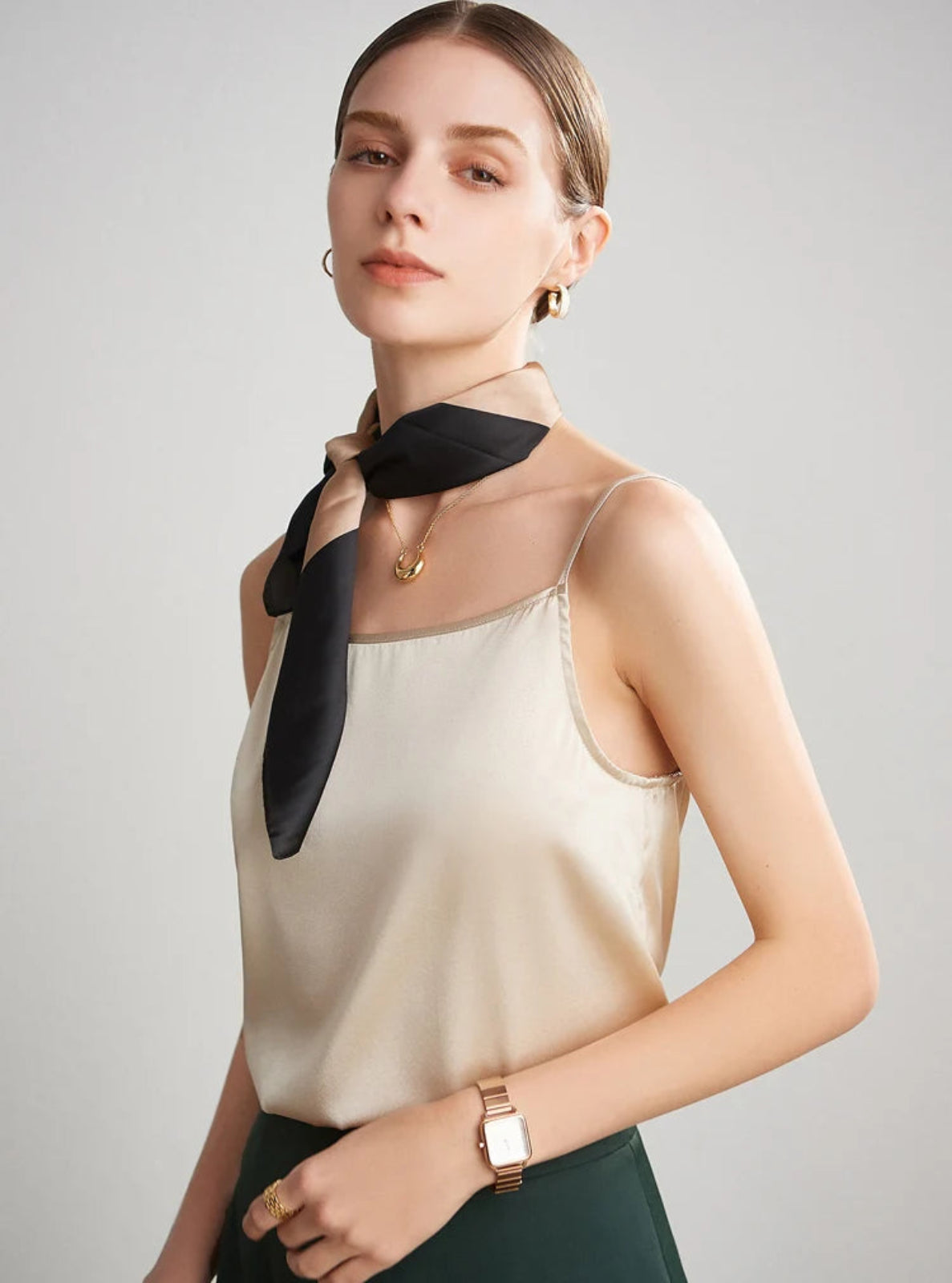 Woman wearing a beige top with a black scarf around her neck against a gray background