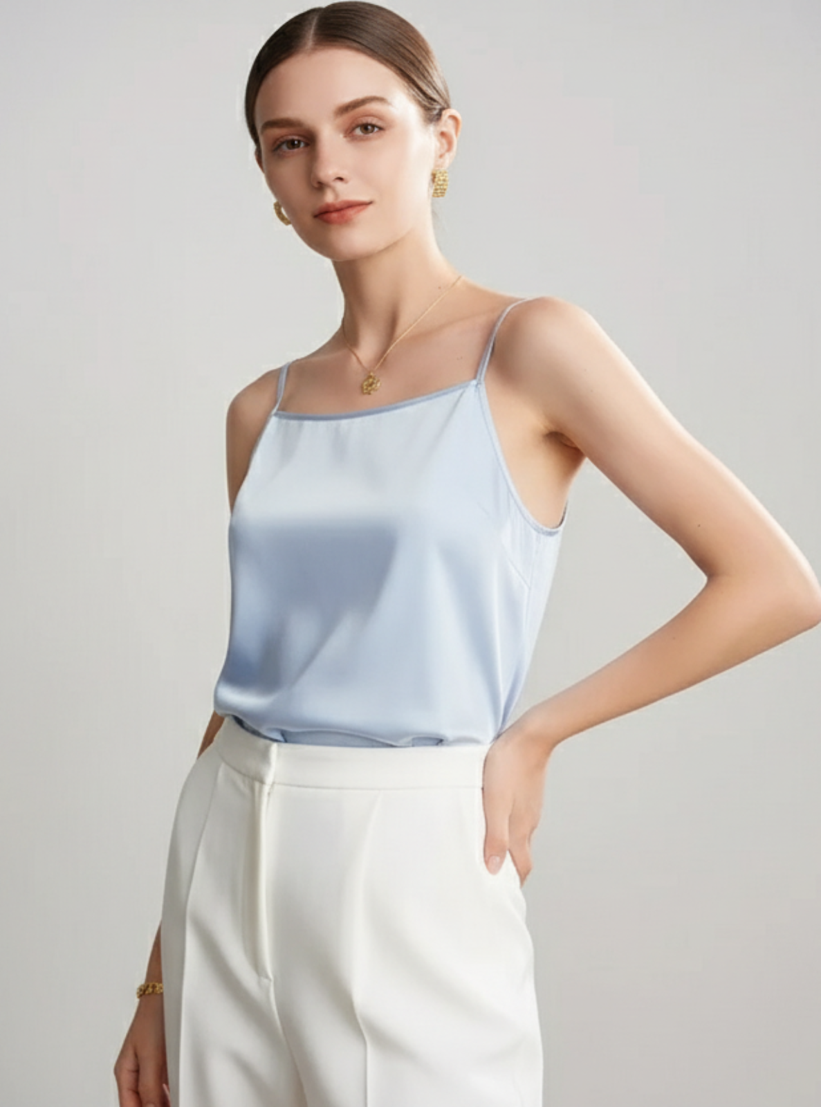 Woman wearing a light blue satin top and white pants on a gray background