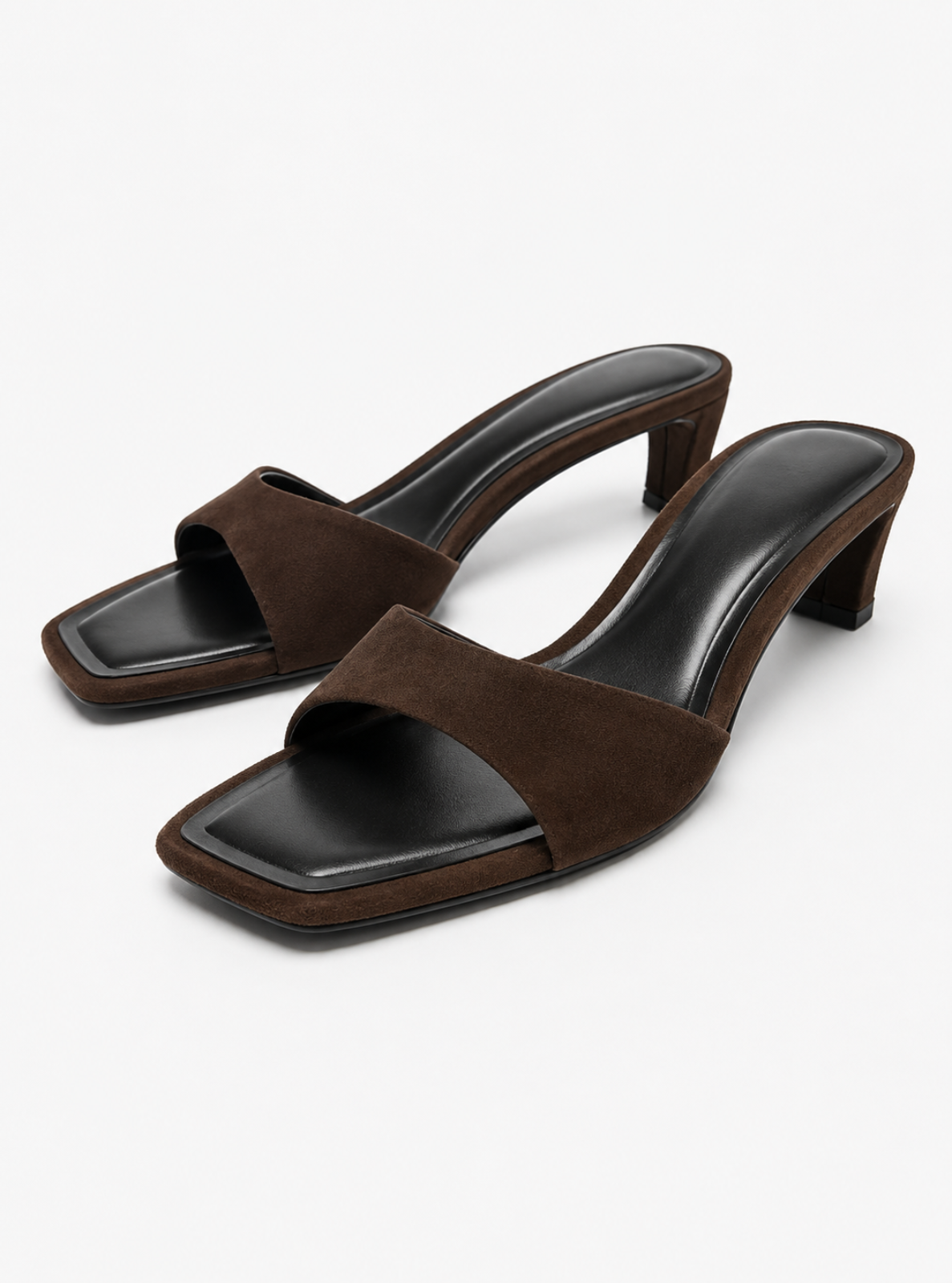 A pair of women's heeled mule sandals in dark brown, featuring a suede-like upper with a single wide strap, square toes, and block heels on a light gray background.