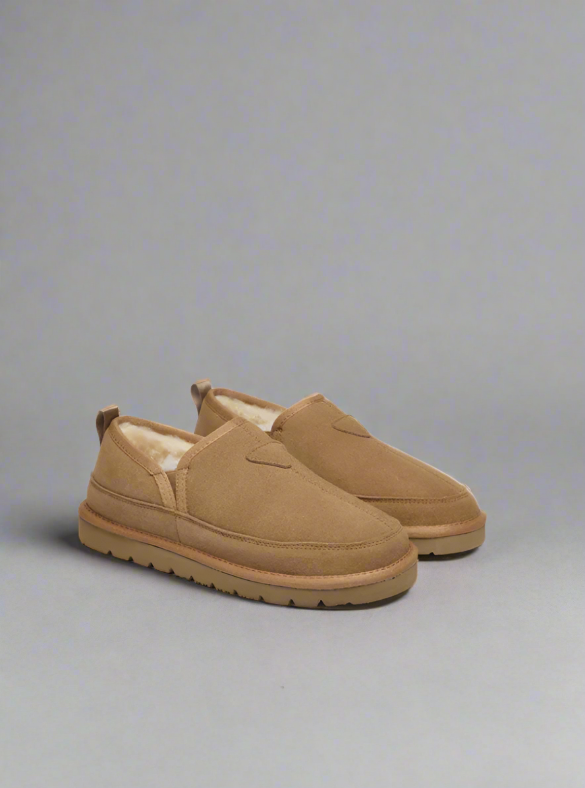 Pair of tan slip-on shoes with fur lining on a gray background
