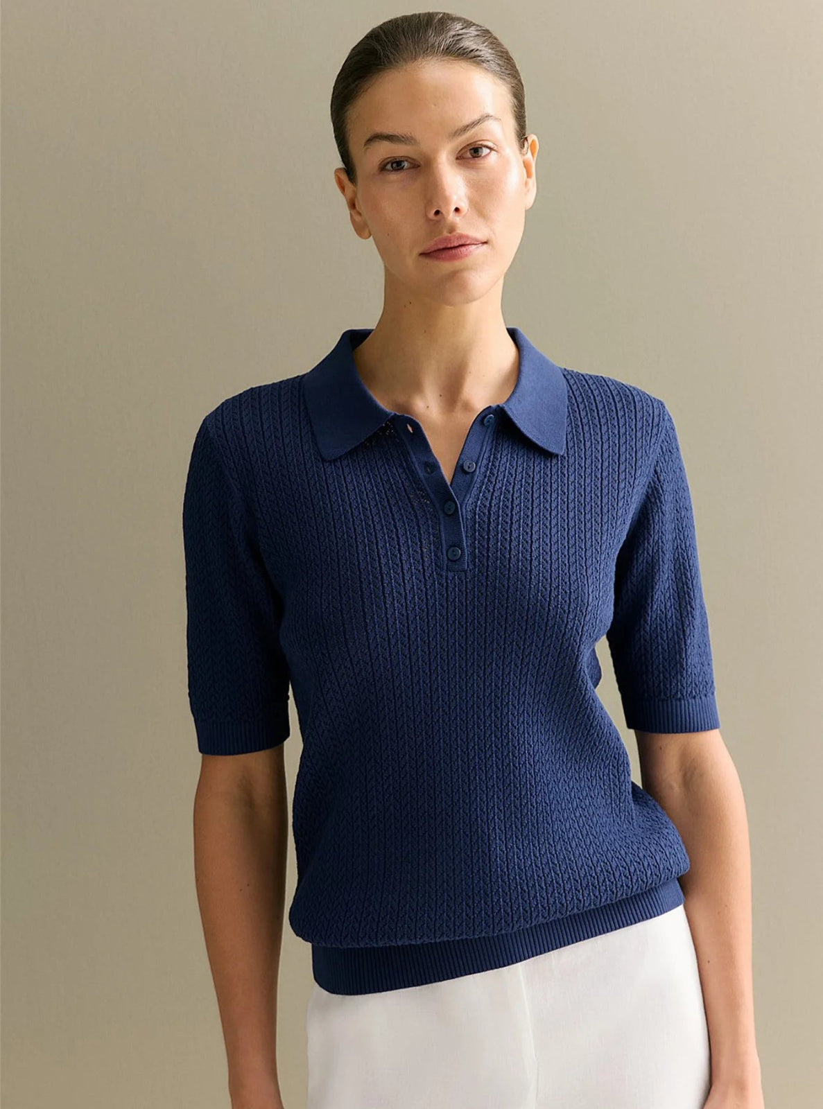 Woman wearing a blue knitted polo shirt against a beige background