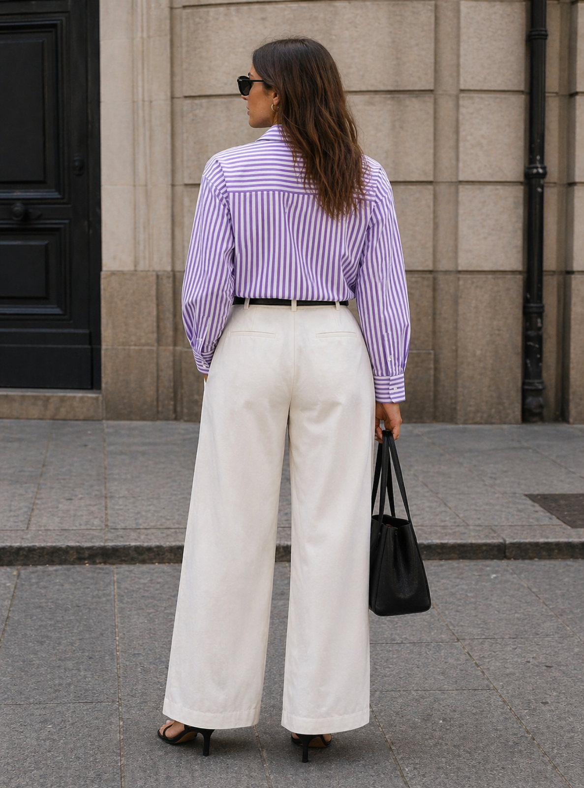 Woman wearing a striped shirt and white pants, standing on a street.