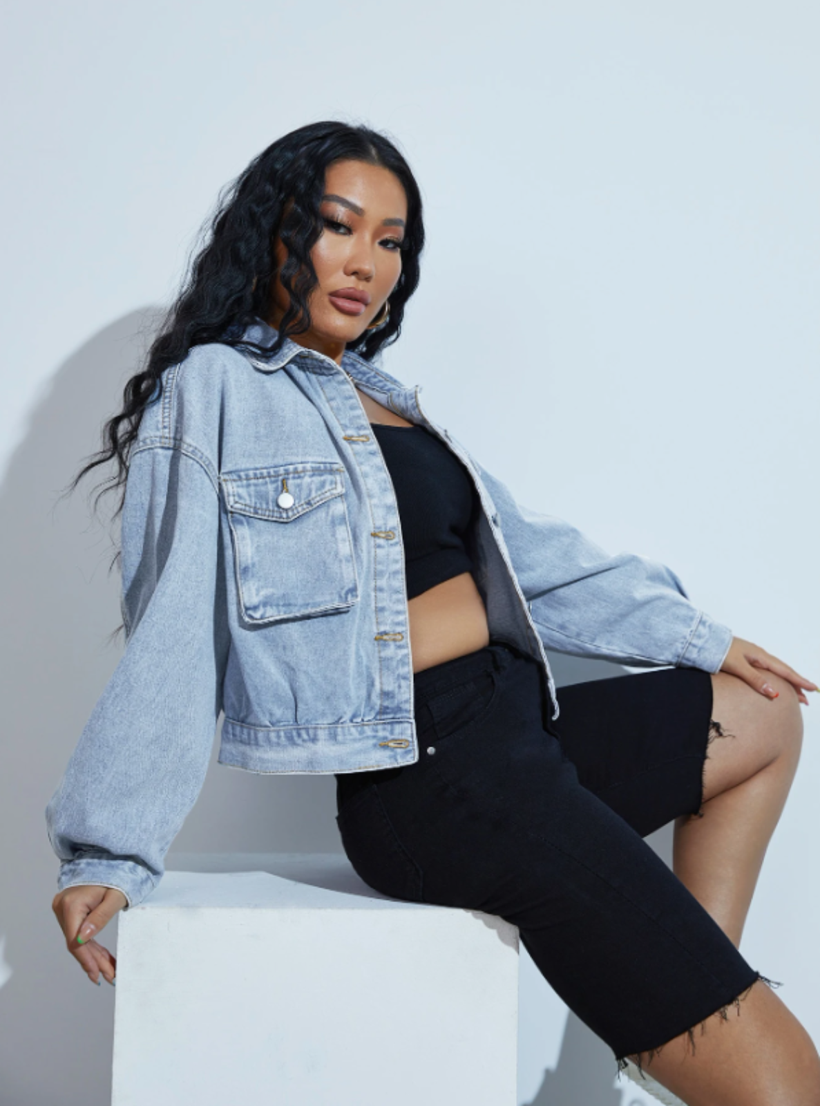 Woman wearing a denim jacket and black outfit against a white background
