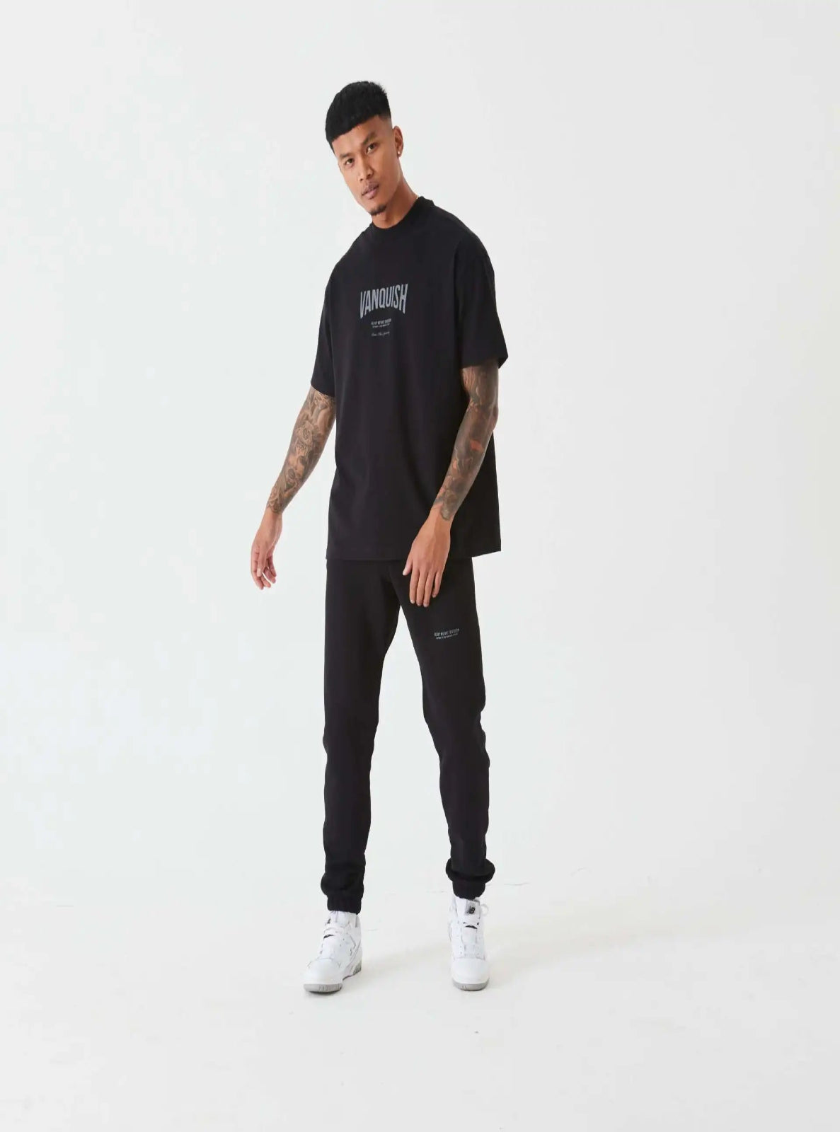 Man wearing a black t-shirt and pants with visible branding on a white background