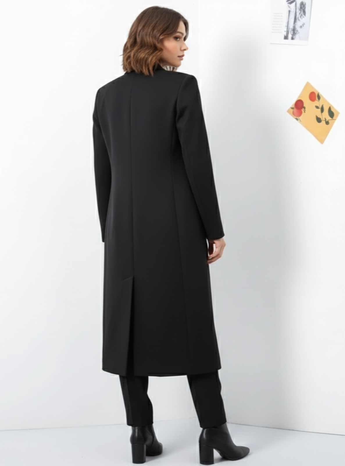 Person wearing a long black coat against a white background