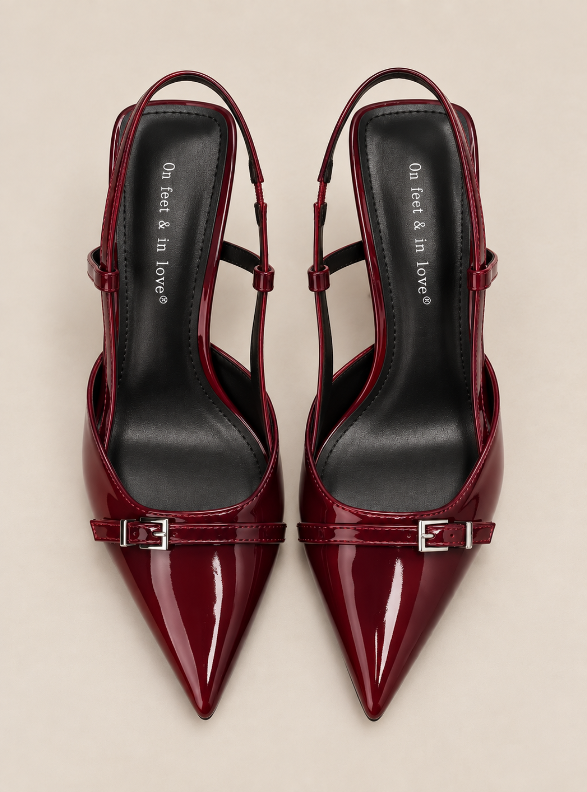A pair of pointed-toe slingback pumps in glossy deep burgundy patent leather, featuring a decorative strap with silver-tone buckles across the toe area and a black insole with white branding text.
