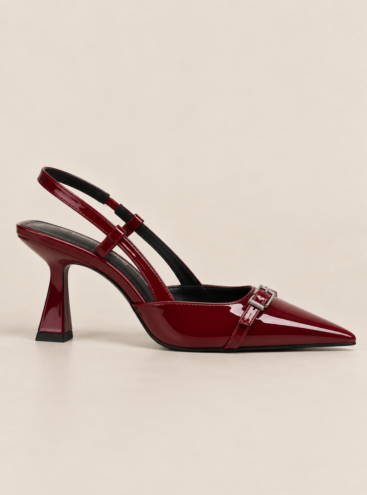 A single patent leather slingback pump in deep burgundy red, featuring a pointed toe, a decorative silver-tone buckle, and a chunky block heel, shown against a solid light beige background.