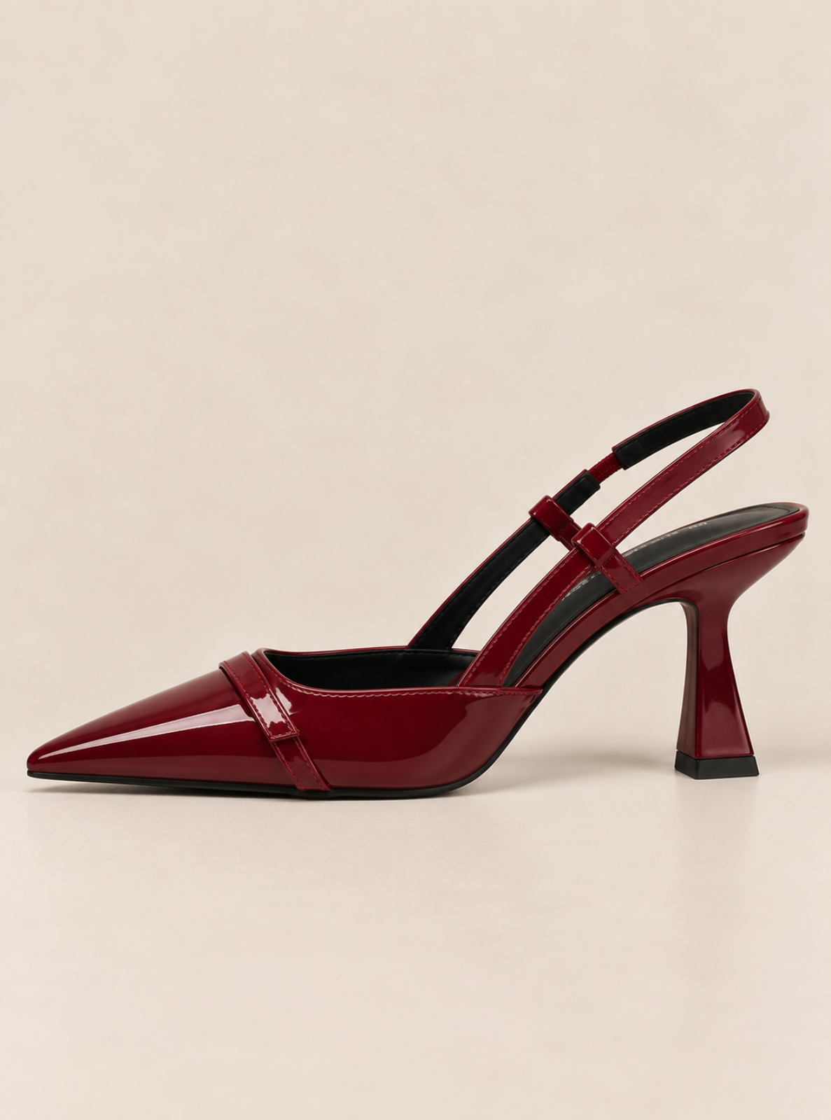 A glossy deep red patent leather slingback pump with a pointed toe and a sculptural flared heel, shown against a solid light beige background.
