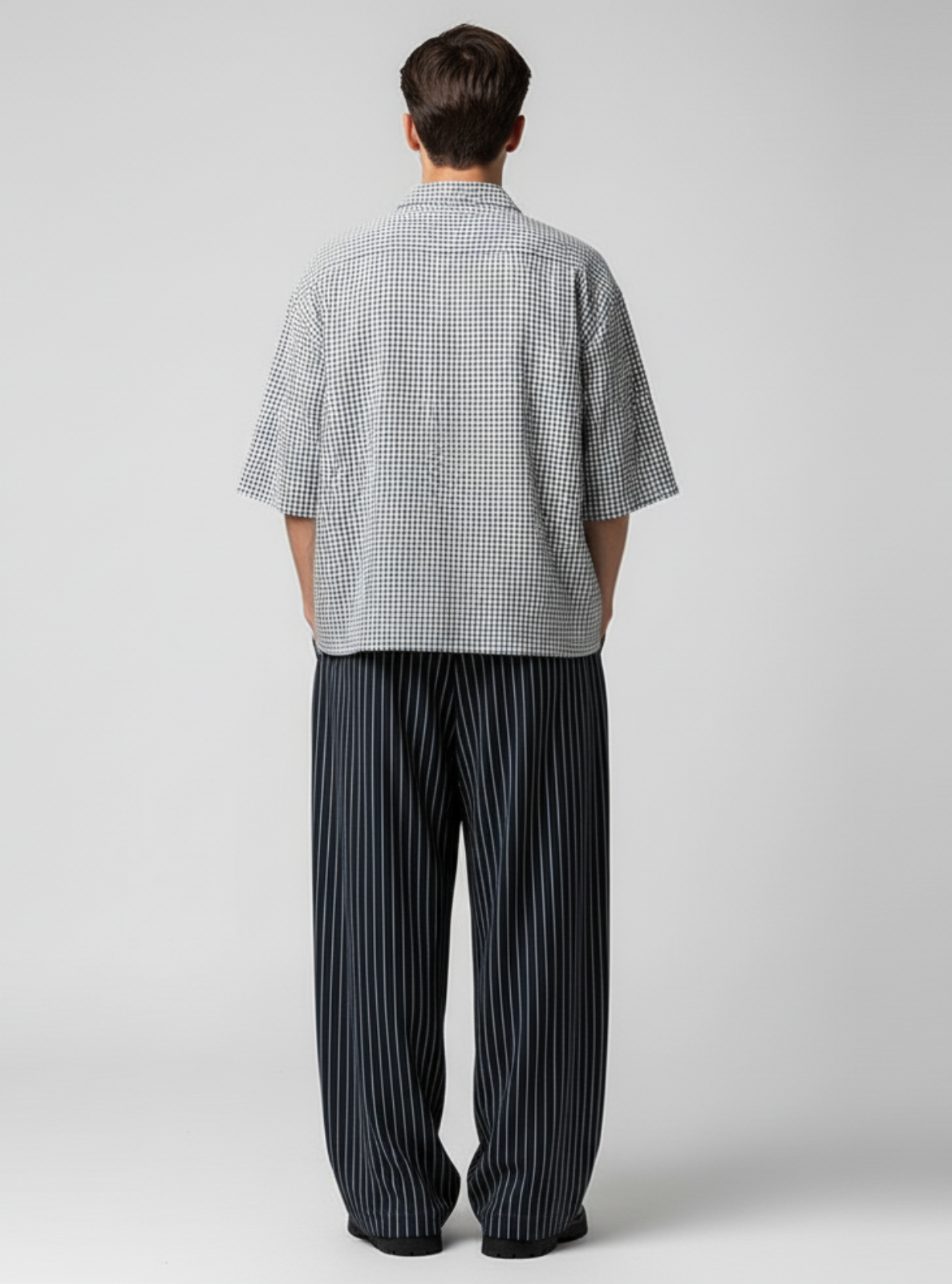 Person wearing a checkered shirt and striped pants on a plain background