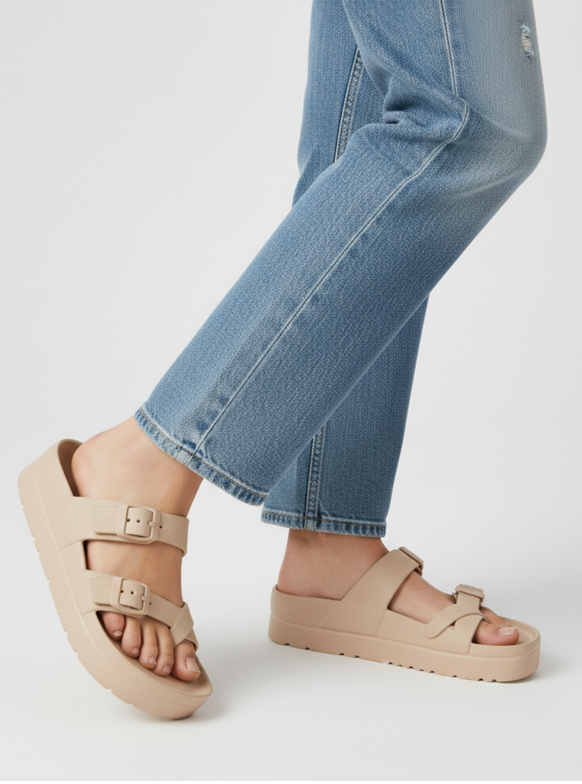 Beige sandals worn with blue jeans on a light gray background