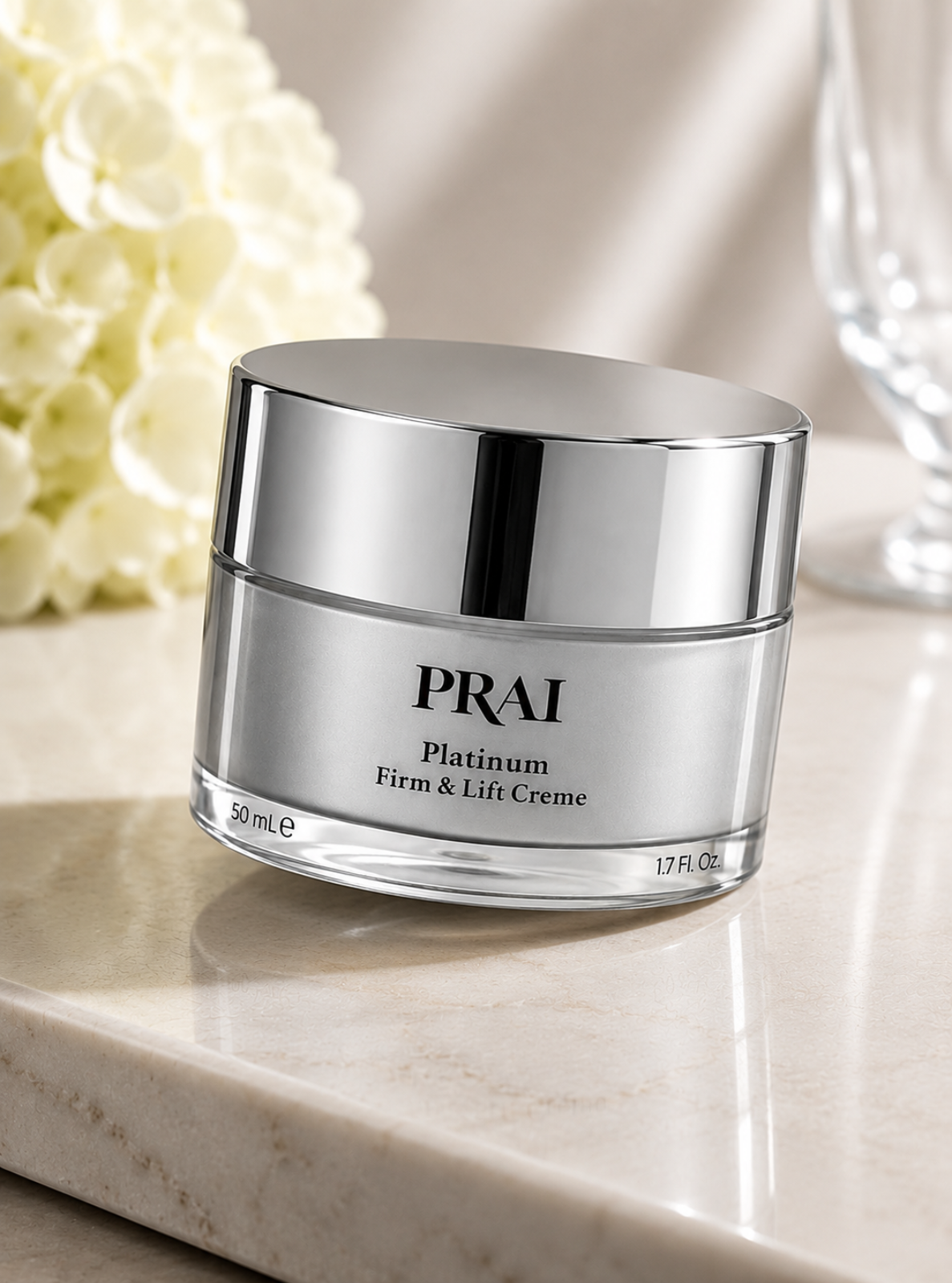 A jar of PRAI Platinum Firm & Lift Creme on a light marble surface with soft-focus white flowers and a glass in the background.