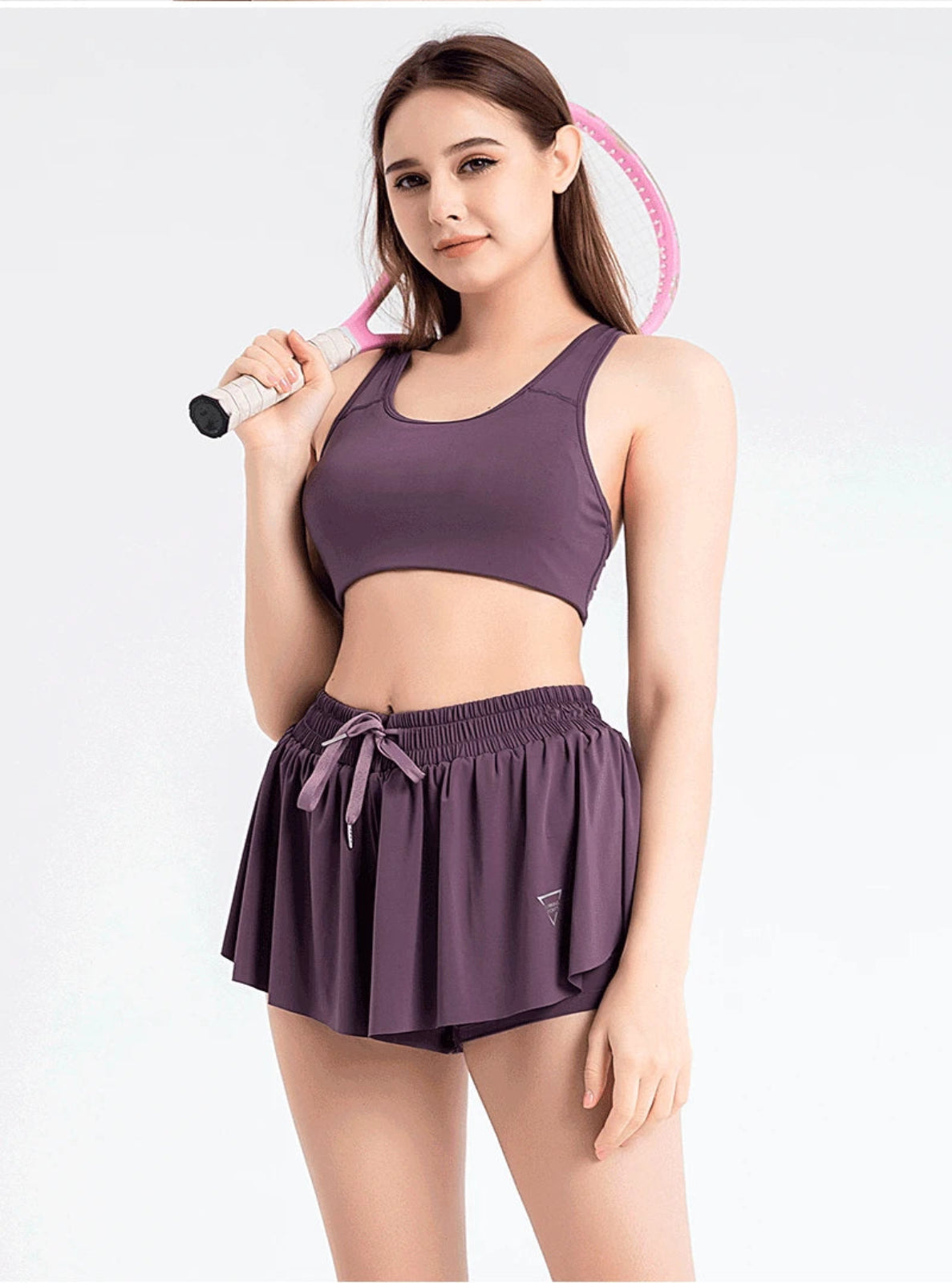 Woman wearing a purple athletic outfit holding a pink and black object on a white background