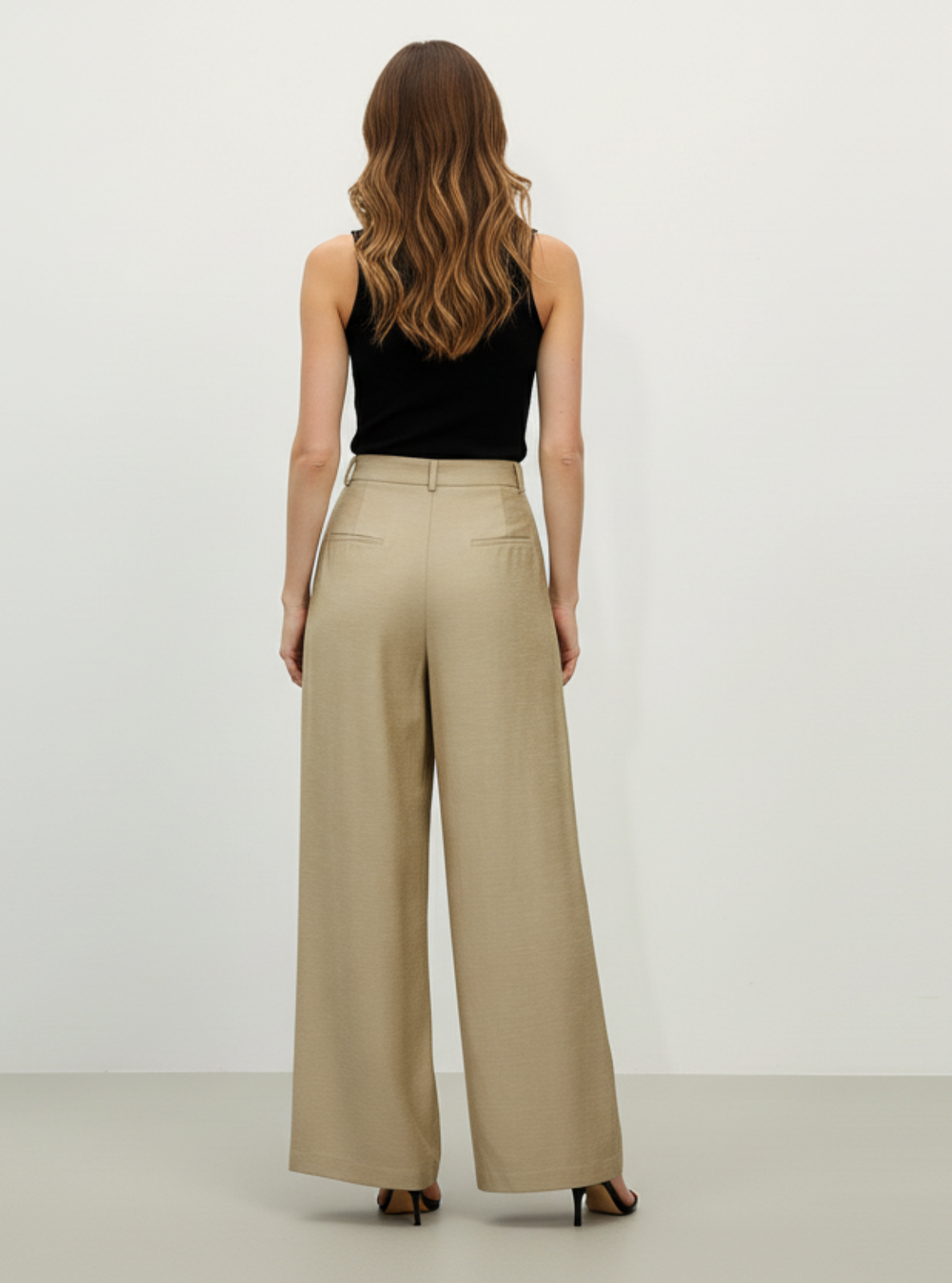 Woman wearing a black top and beige wide-leg pants on a white background