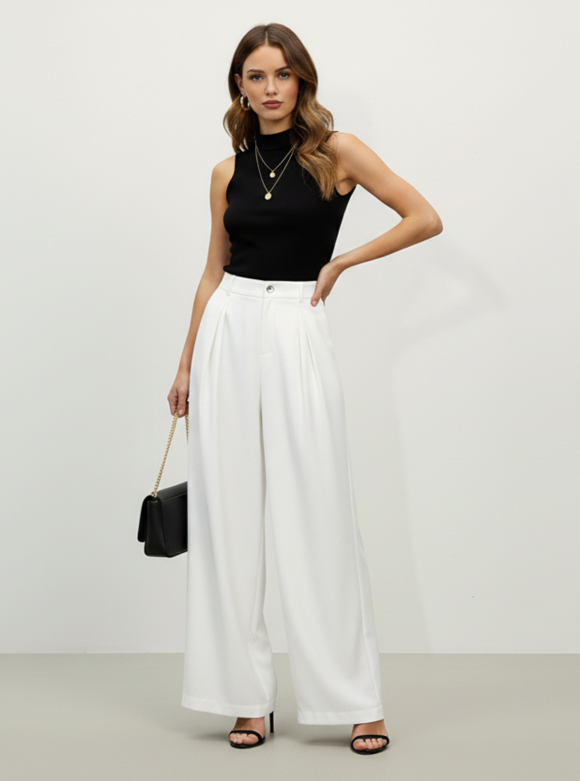Woman wearing a black sleeveless top and white wide-leg pants against a plain background
