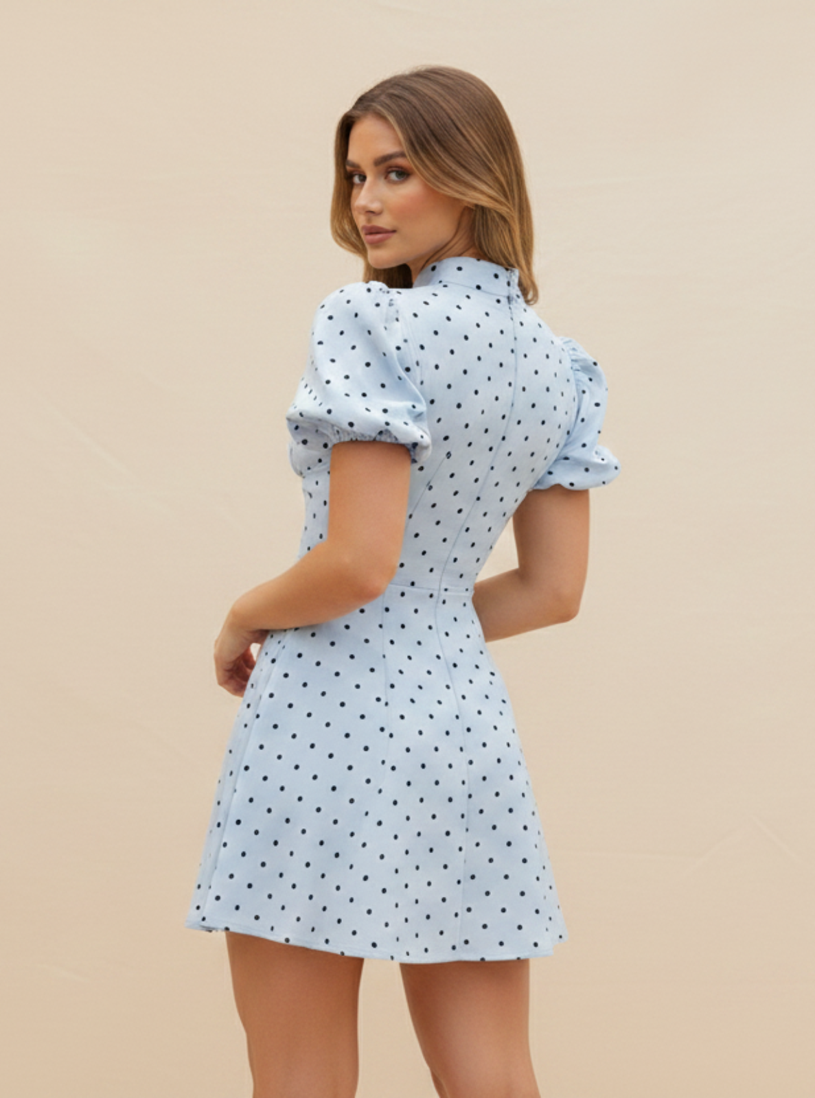 Woman wearing a light blue polka dot dress against a beige background