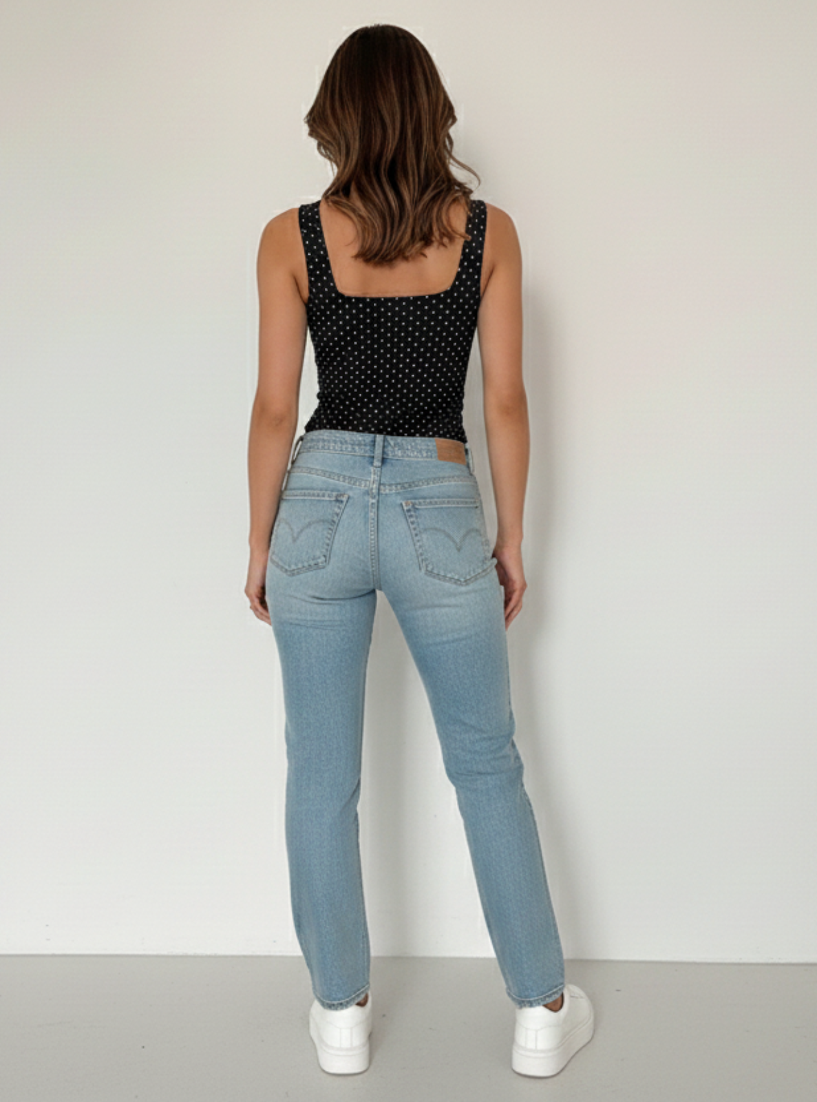 Woman wearing light blue jeans and a black polka dot top against a white background