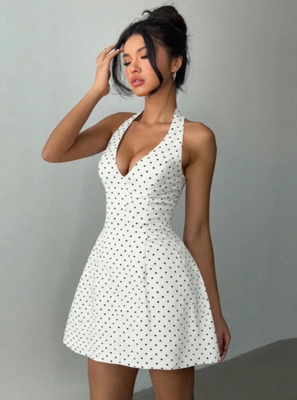 Woman wearing a white dress with black polka dots against a gray background