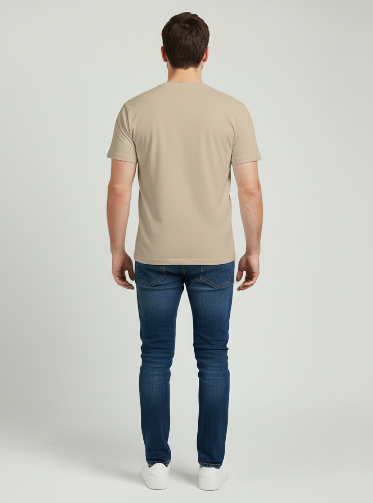 Man wearing a beige t-shirt and blue jeans on a light gray background