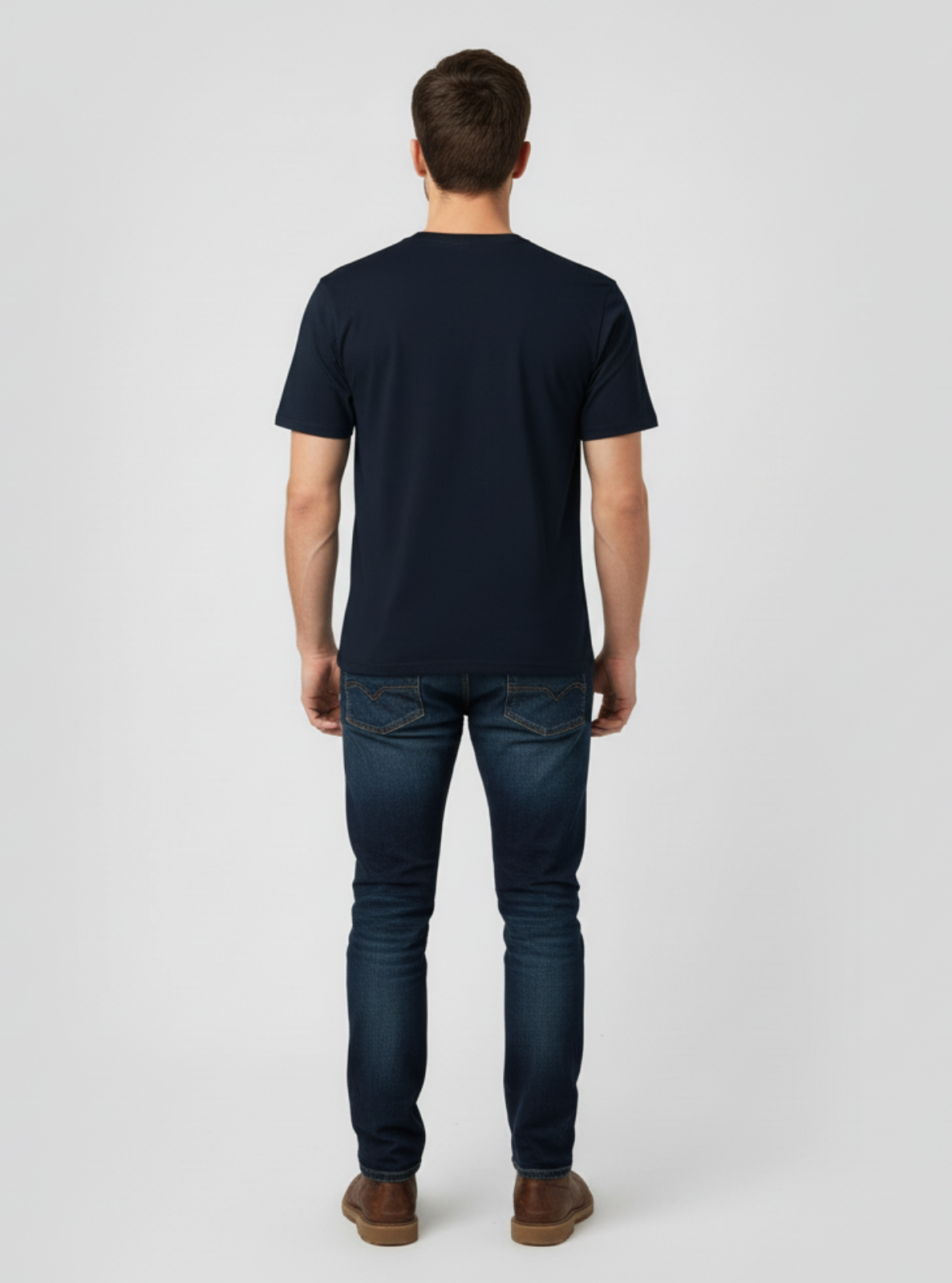 Man wearing a navy t-shirt and dark jeans on a white background
