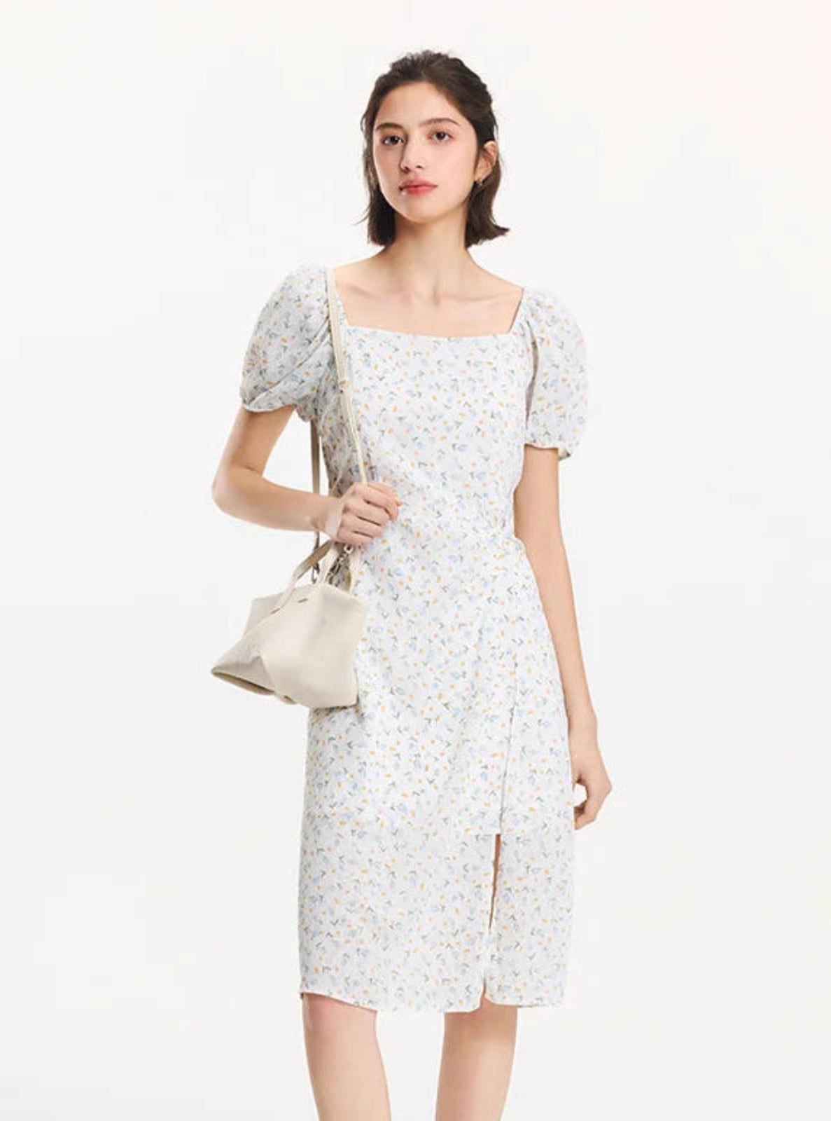 Woman wearing a floral dress holding a beige handbag on a white background