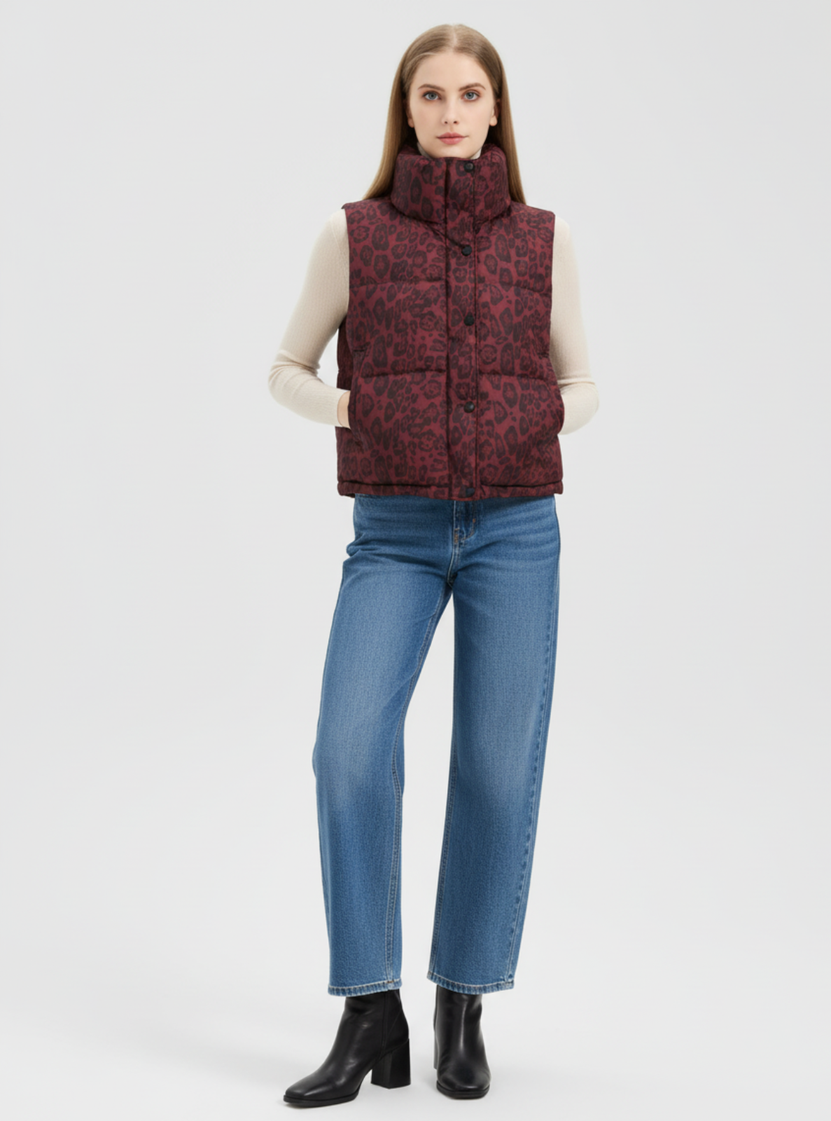 Woman wearing a patterned red vest, blue jeans, and black boots on a white background