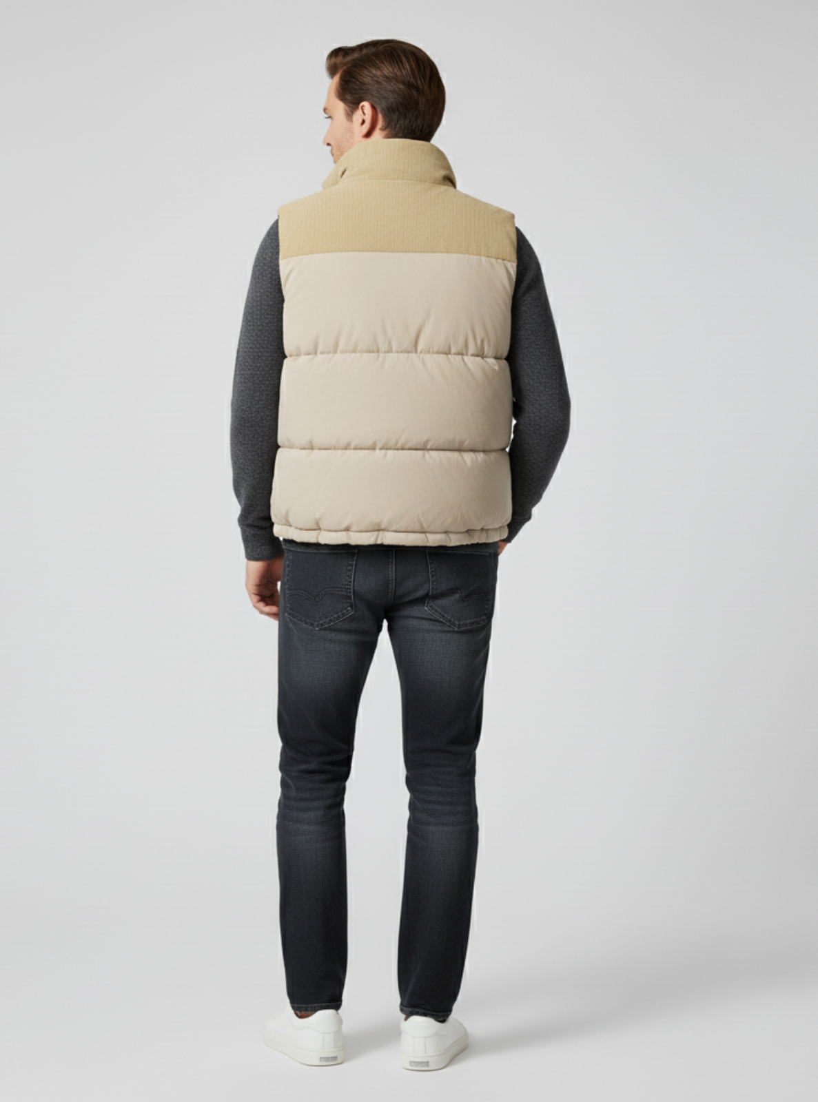 Man wearing a beige puffer vest over a dark long-sleeve shirt and jeans on a light gray background