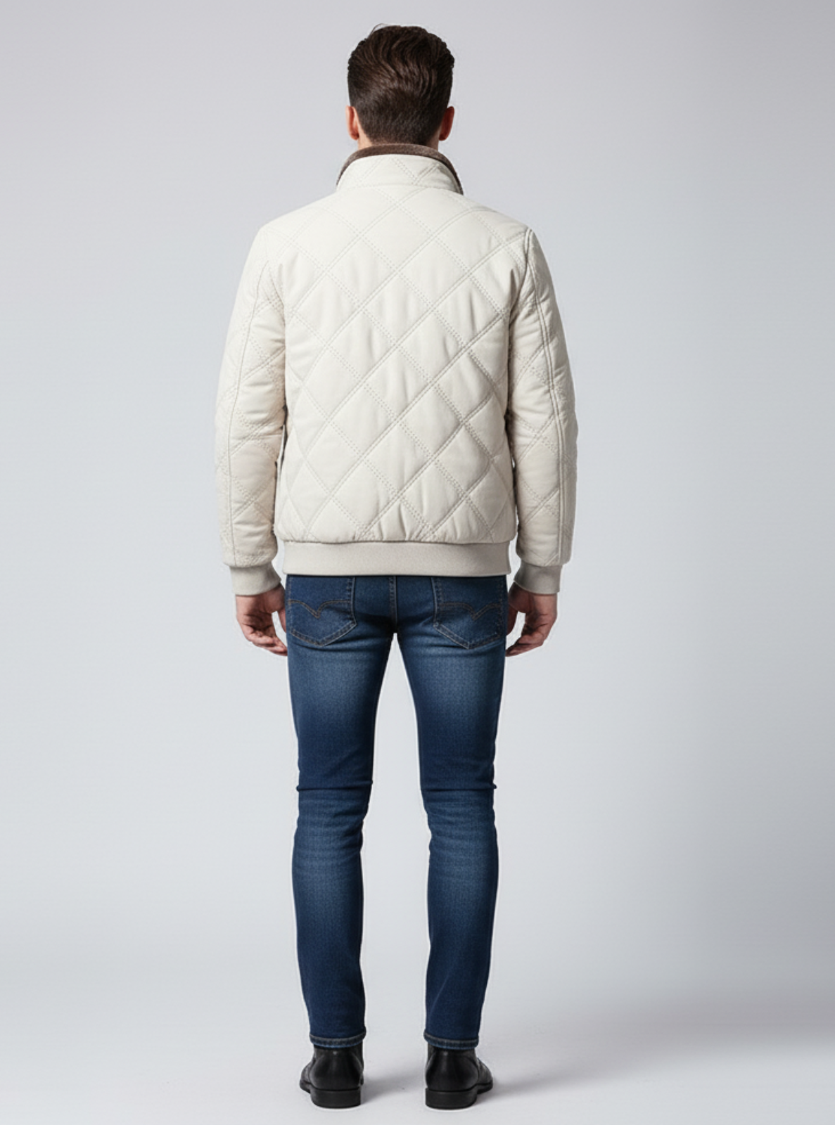 Man wearing a beige quilted jacket and blue jeans on a white background