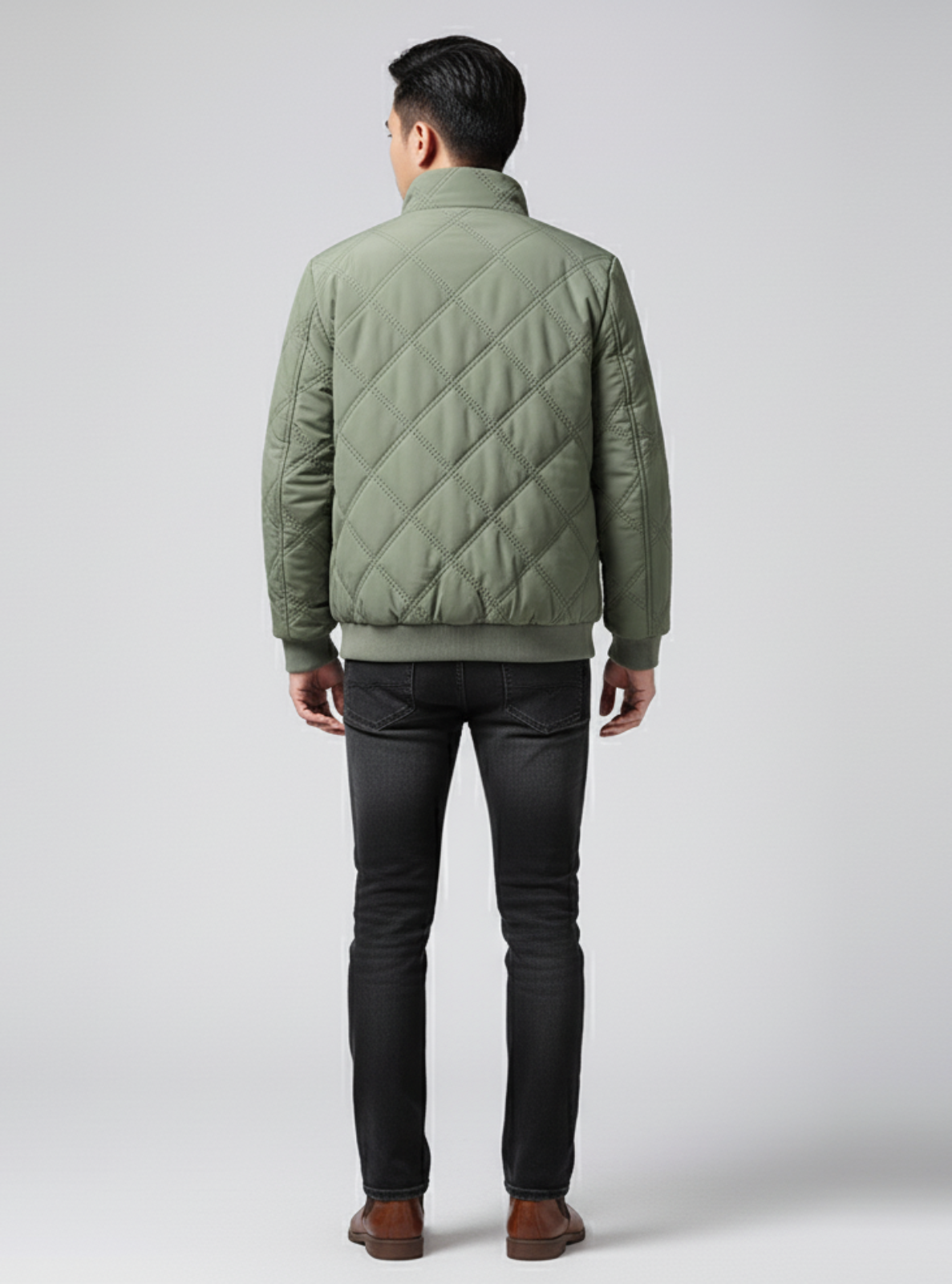 Person wearing a green quilted jacket and dark jeans on a white background