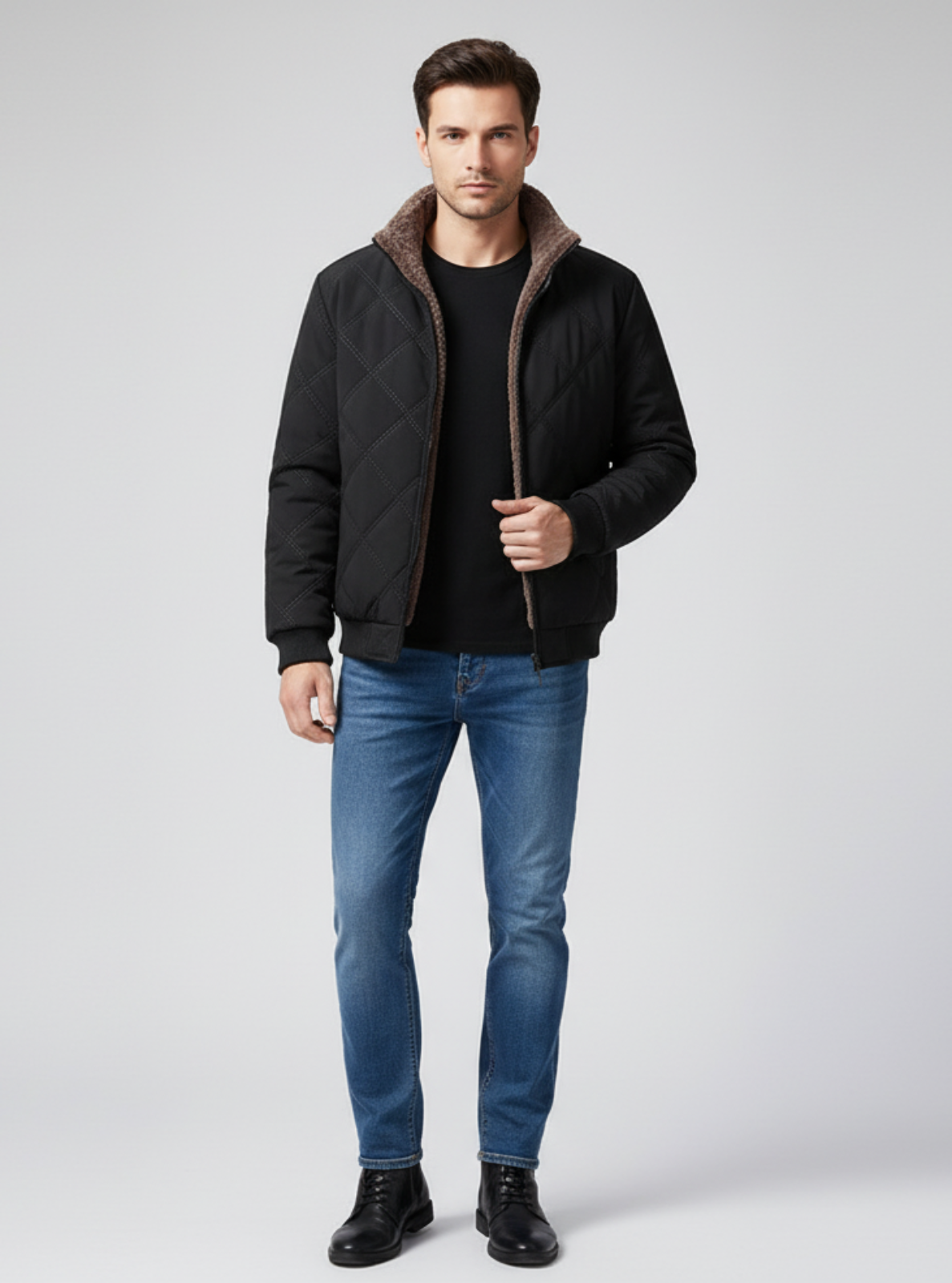 Man wearing a black quilted jacket, black shirt, blue jeans, and black shoes on a light gray background