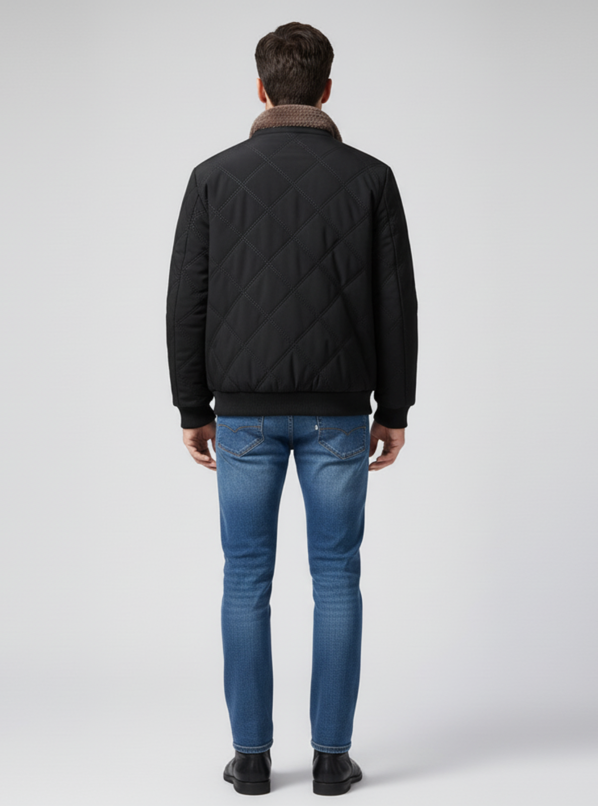 Man wearing a black quilted jacket and blue jeans on a white background