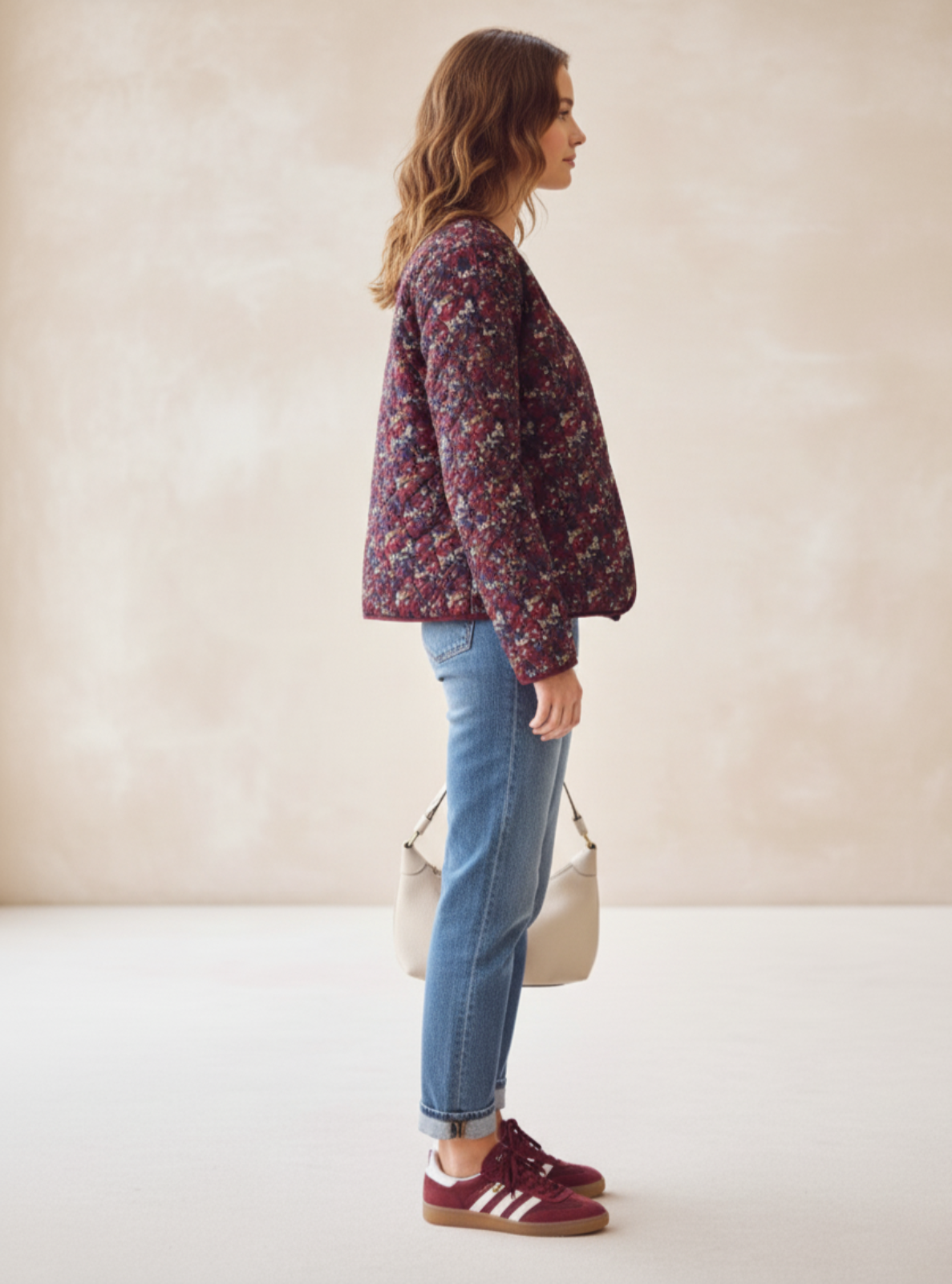 Woman wearing a floral jacket, blue jeans, and maroon shoes against a beige background