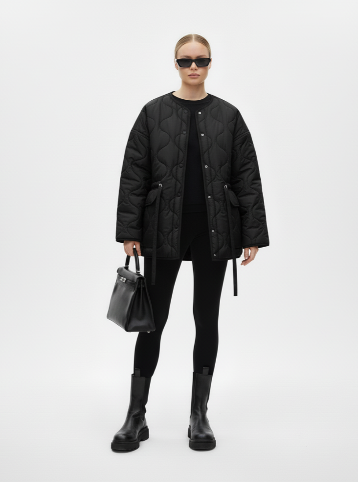 Person wearing a black quilted jacket and holding a black handbag on a white background