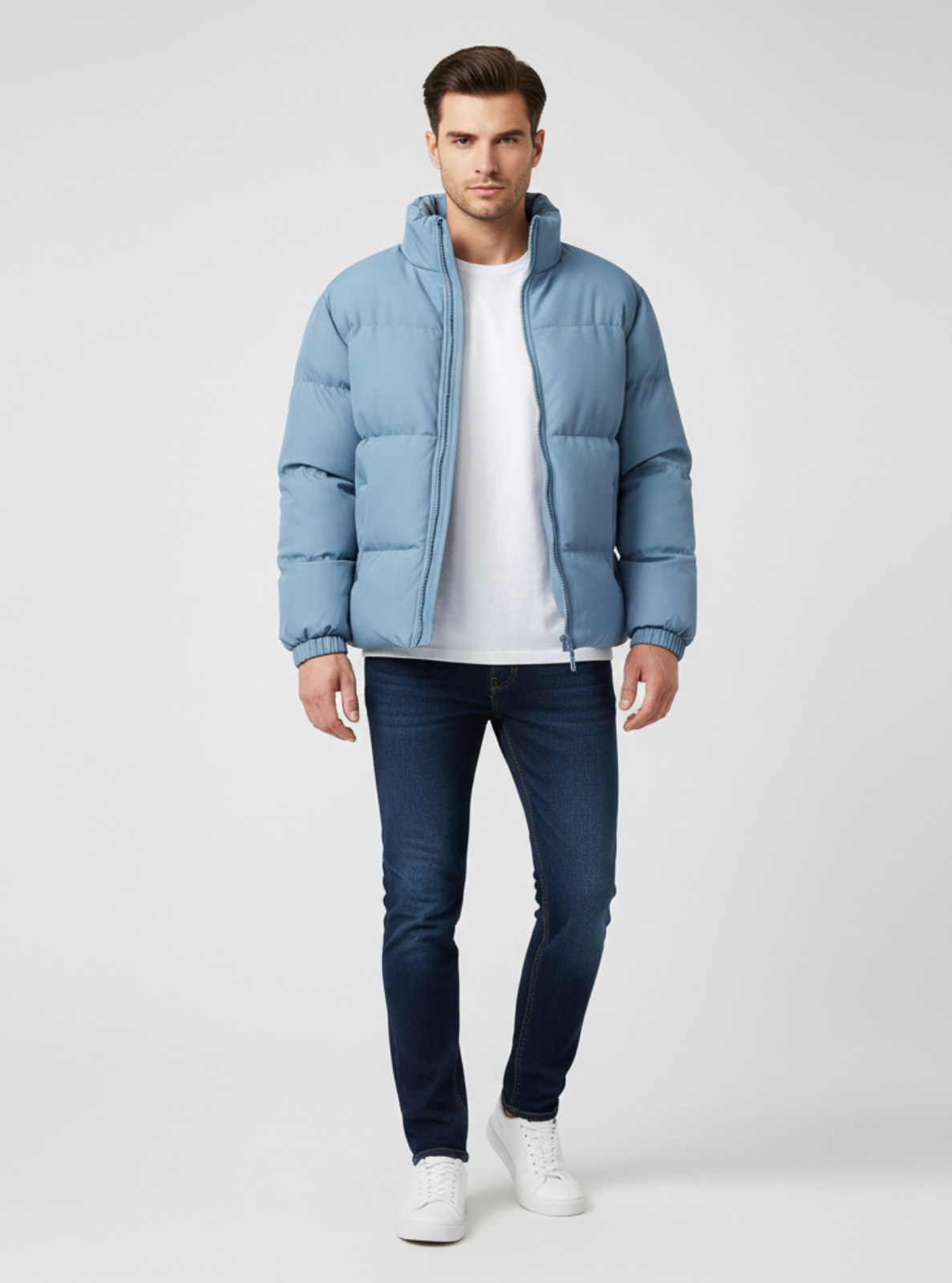 Man wearing a light blue puffer jacket, white shirt, dark jeans, and white sneakers on a white background