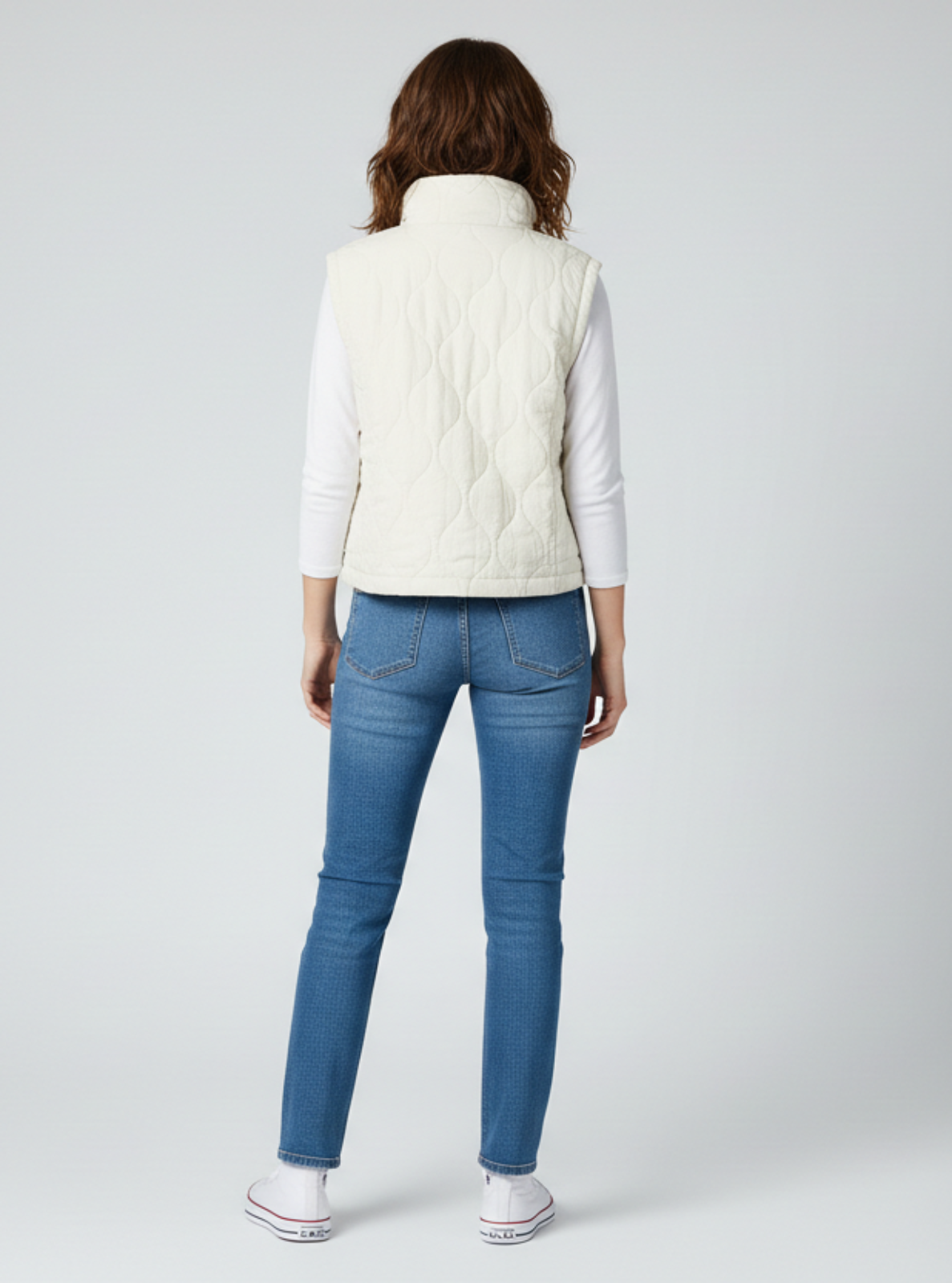Person wearing a white jacket and blue jeans on a gray background