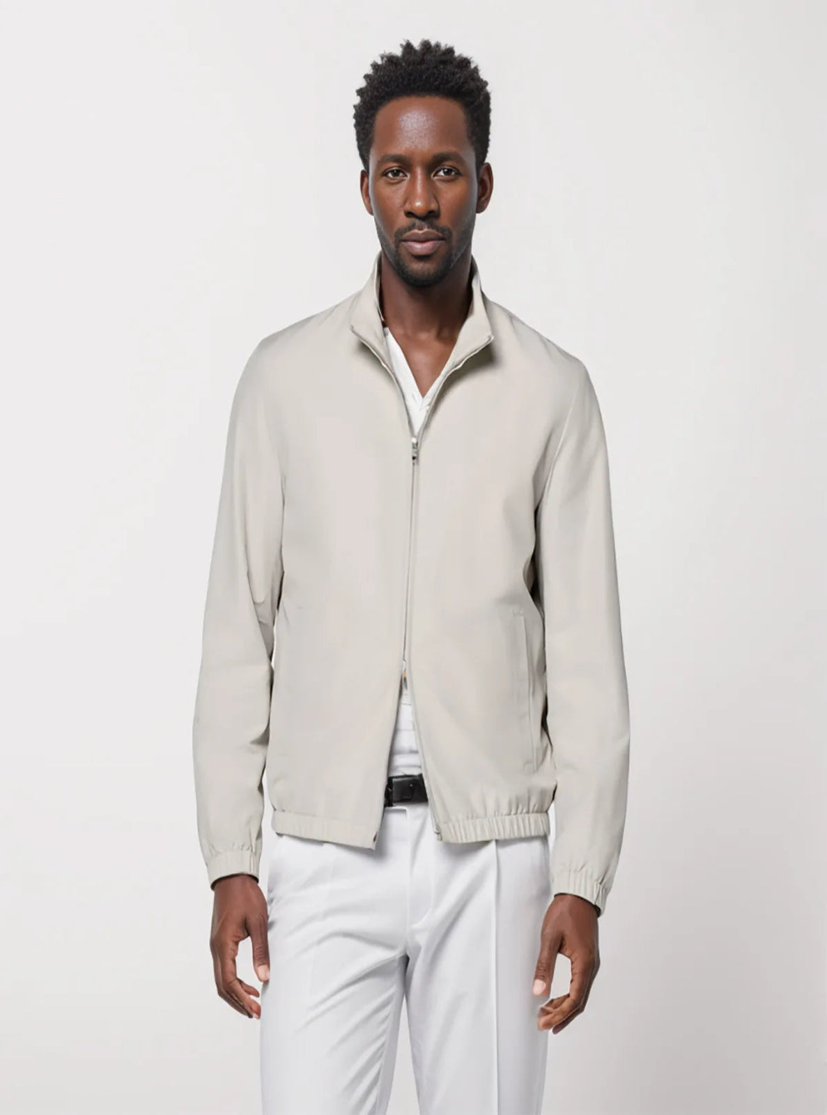 Man wearing a light gray zip-up sweater over a white shirt with white pants on a light gray background