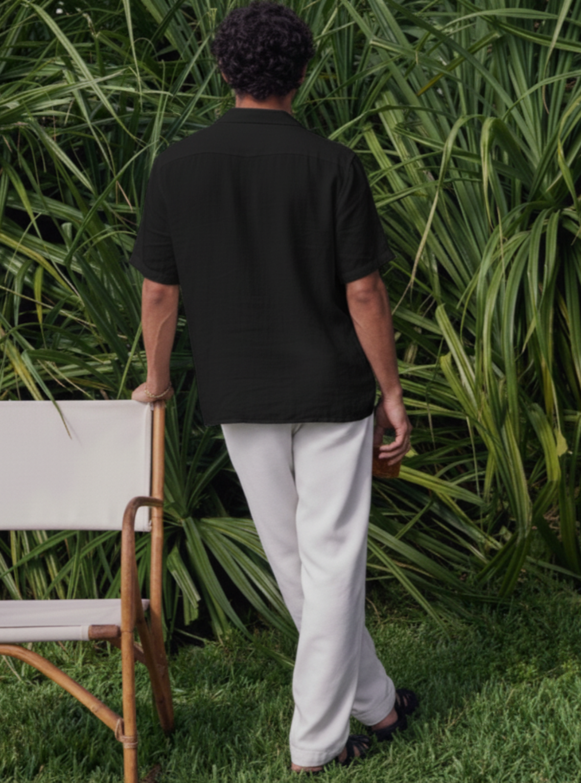 Person wearing a black shirt and white pants standing in front of green foliage