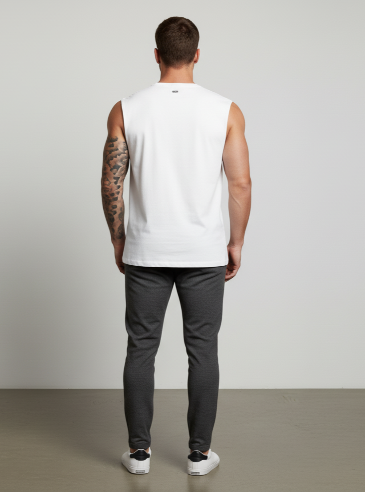 Man wearing a white sleeveless shirt and dark pants against a plain background