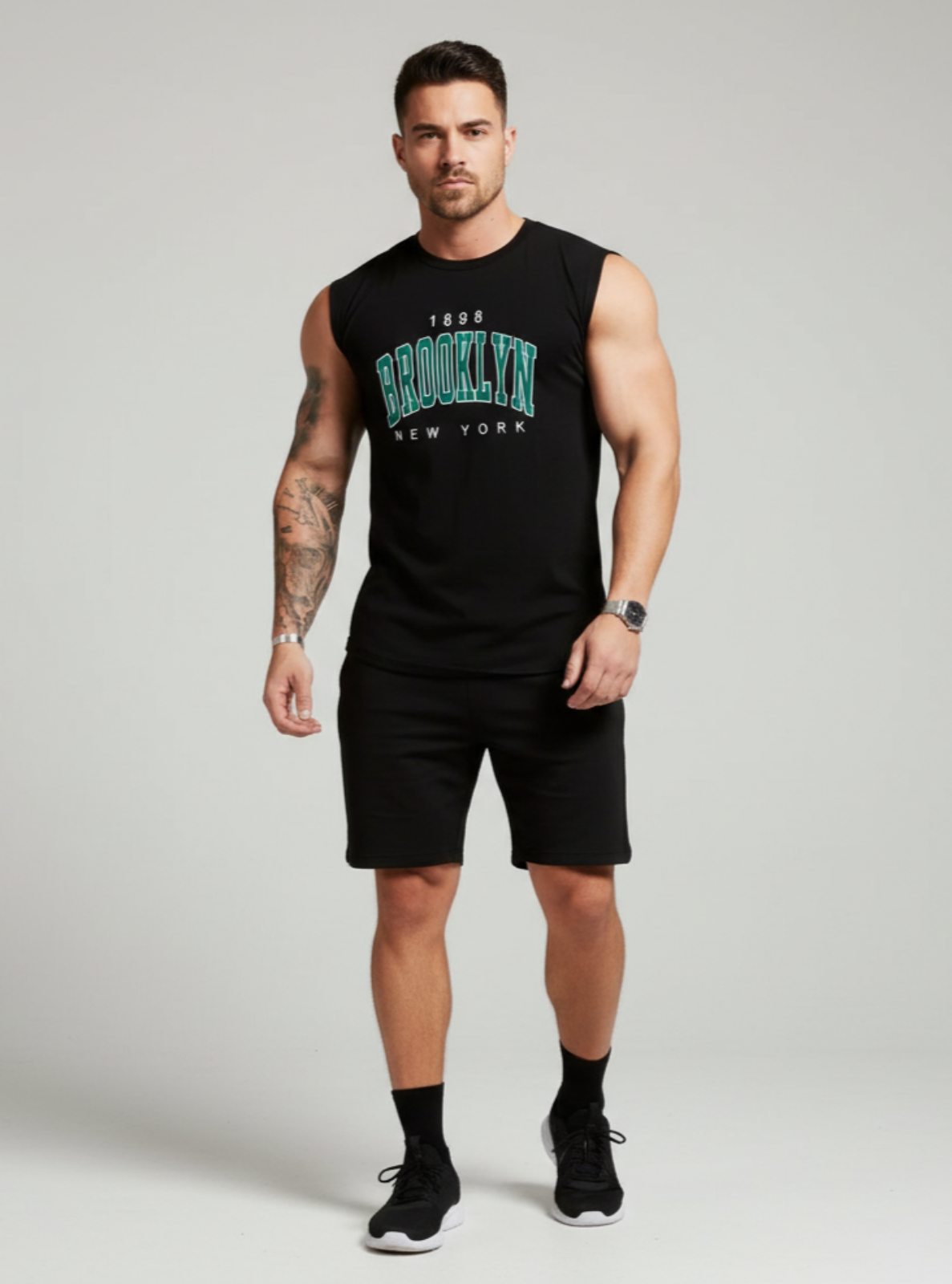Man wearing a black sleeveless shirt with text and black shorts on a gray background