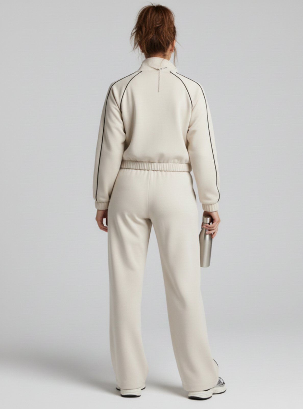 Person wearing a beige tracksuit holding a silver phone on a white background