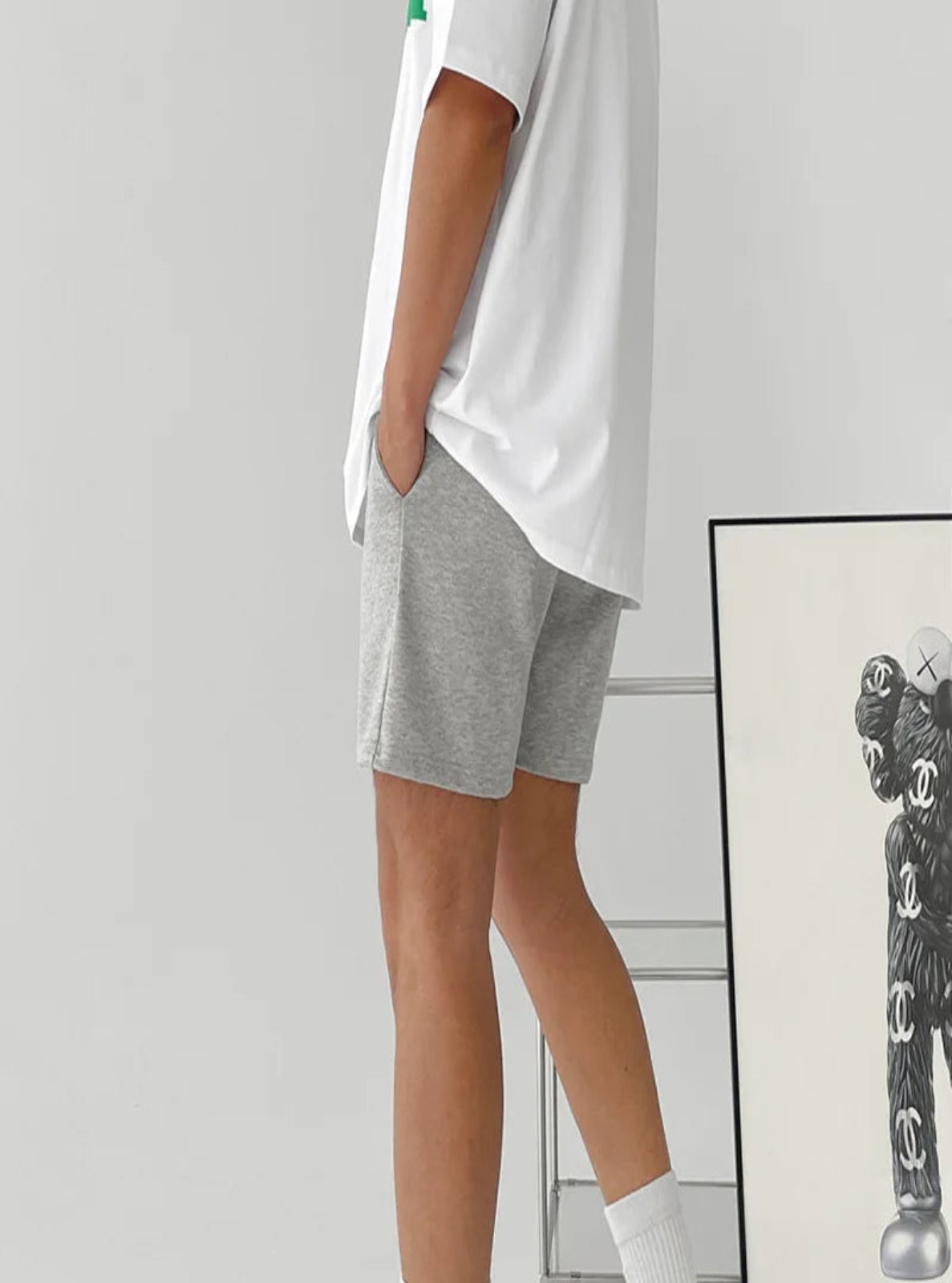 Person wearing gray shorts and a white shirt with a minimal background