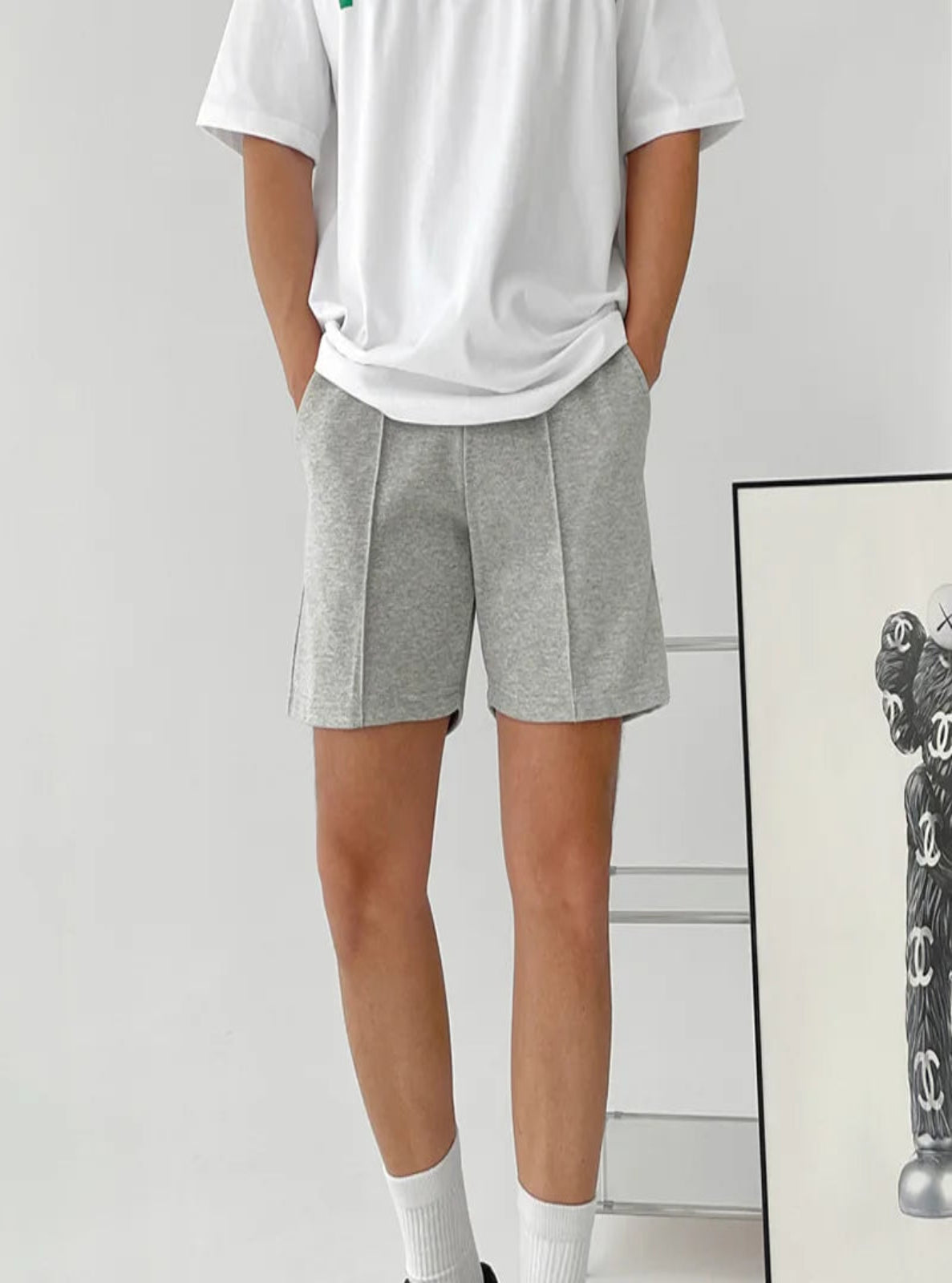 Person wearing gray shorts and a white t-shirt against a plain background