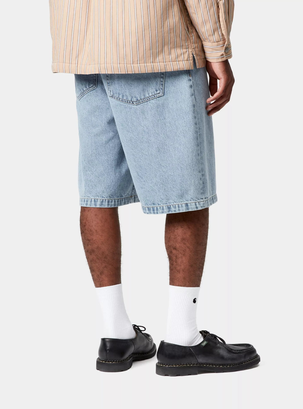 Person wearing light blue denim shorts, white socks, and black shoes on a white background